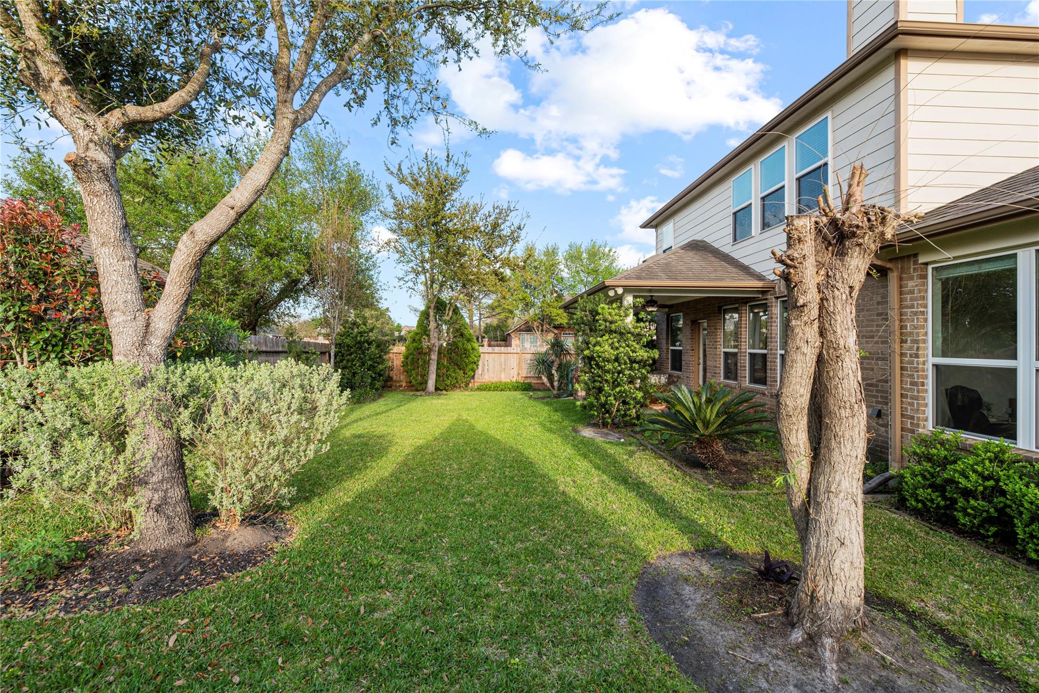 Backyard lawn with mature trees and shrubs beside the two-story house and covered patio.