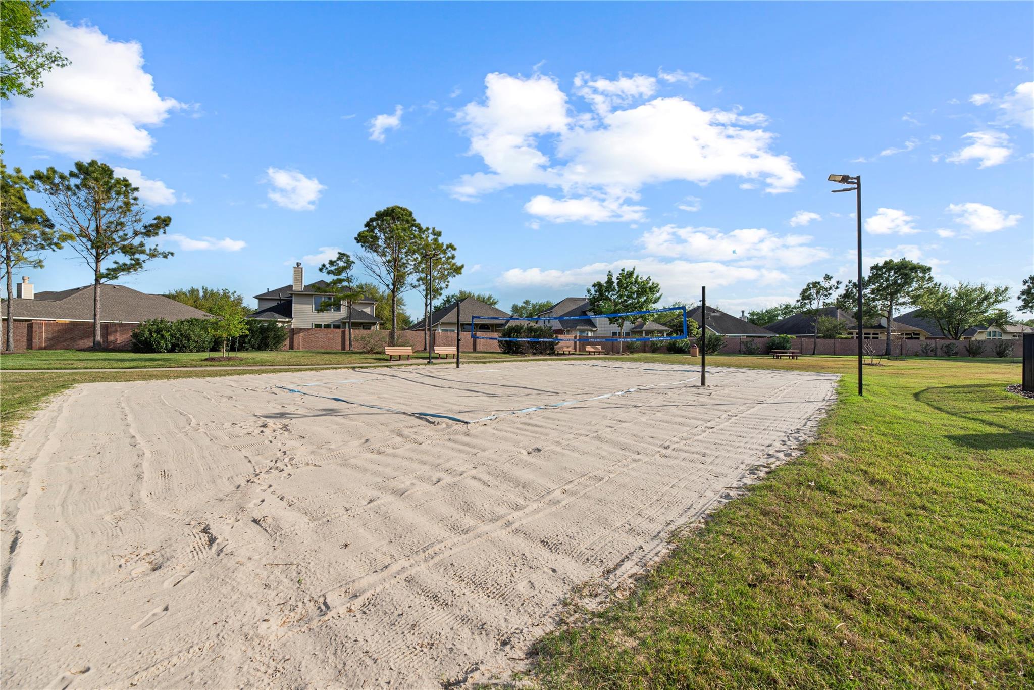 Sandy volleyball court with a blue net, benches, and homes in the background.
