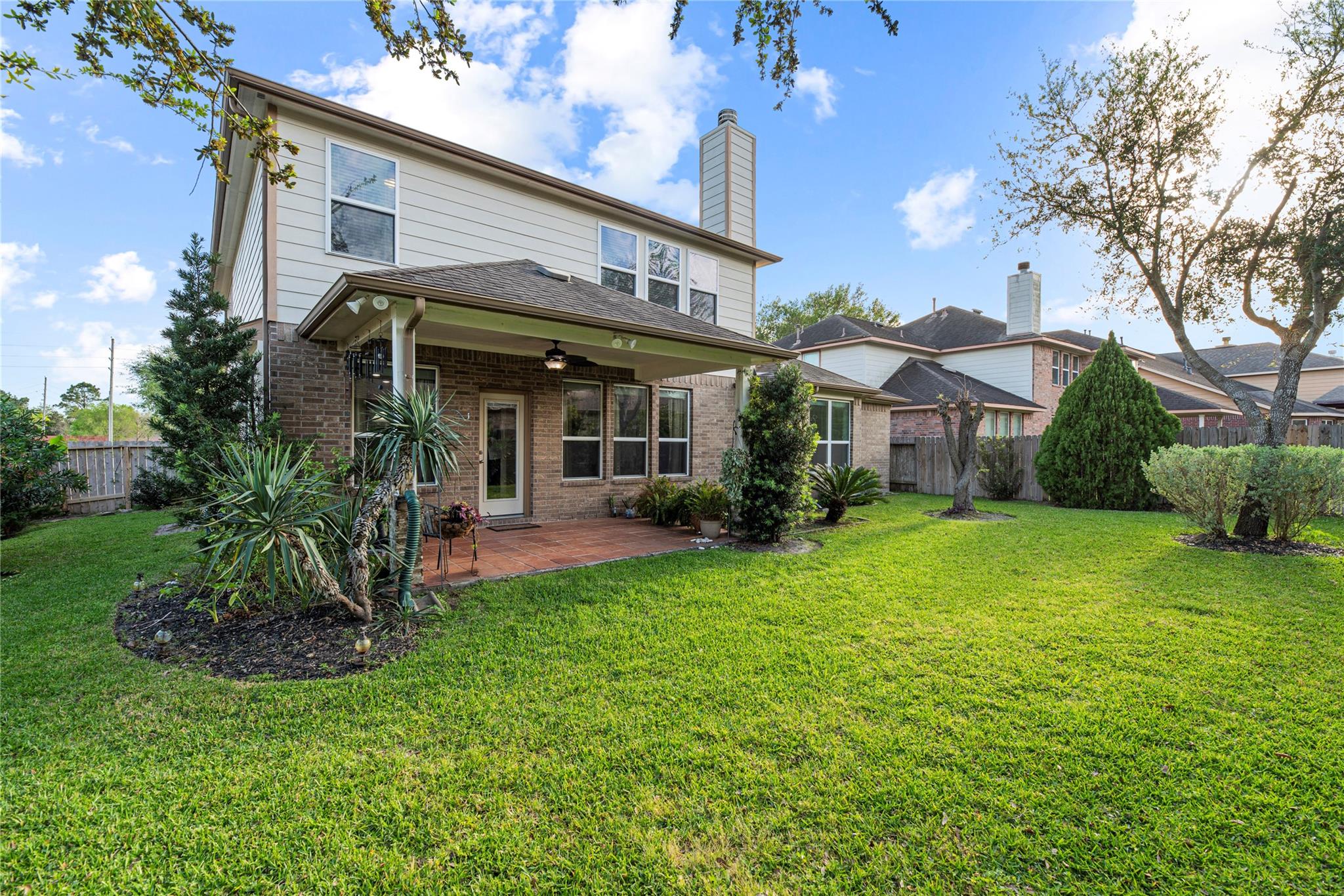 Two-story home with a covered brick patio and spacious green backyard.