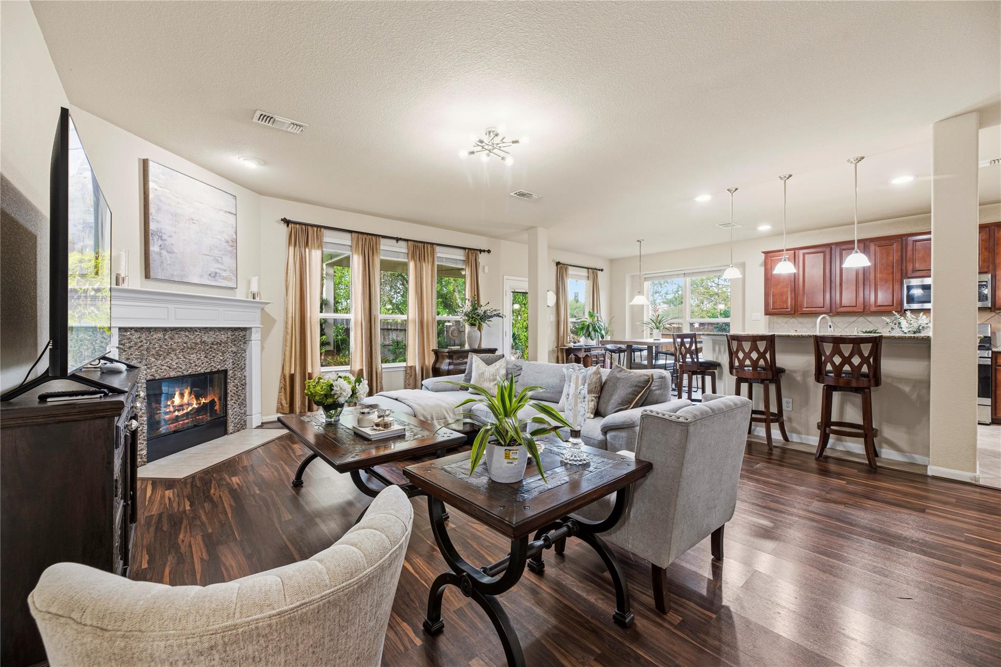 Open-plan living room with a fireplace, gray sectional, and kitchen island with bar stools.