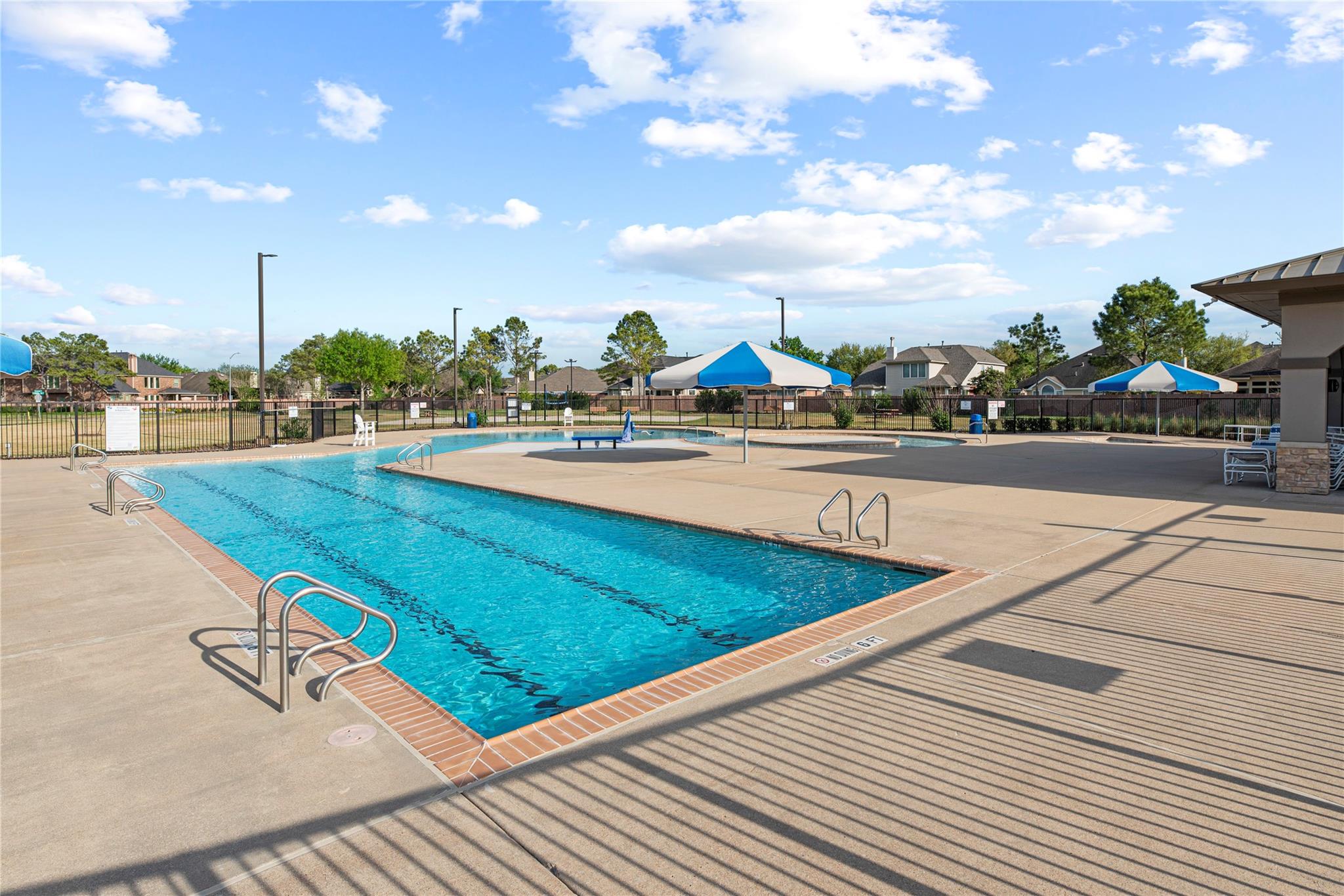 Community swimming pool with blue-and-white shade umbrellas and a spacious concrete deck.