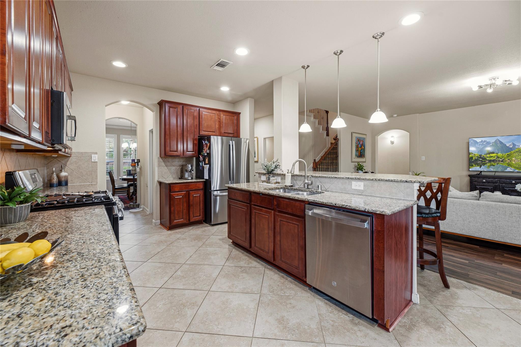 Open kitchen with dark wood cabinets, granite island, stainless appliances, and adjoining living area.
