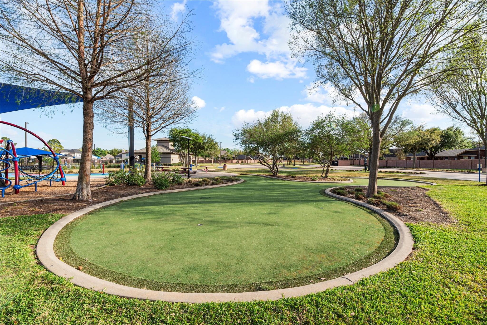 Community putting green bordered by trees, with a playground nearby.