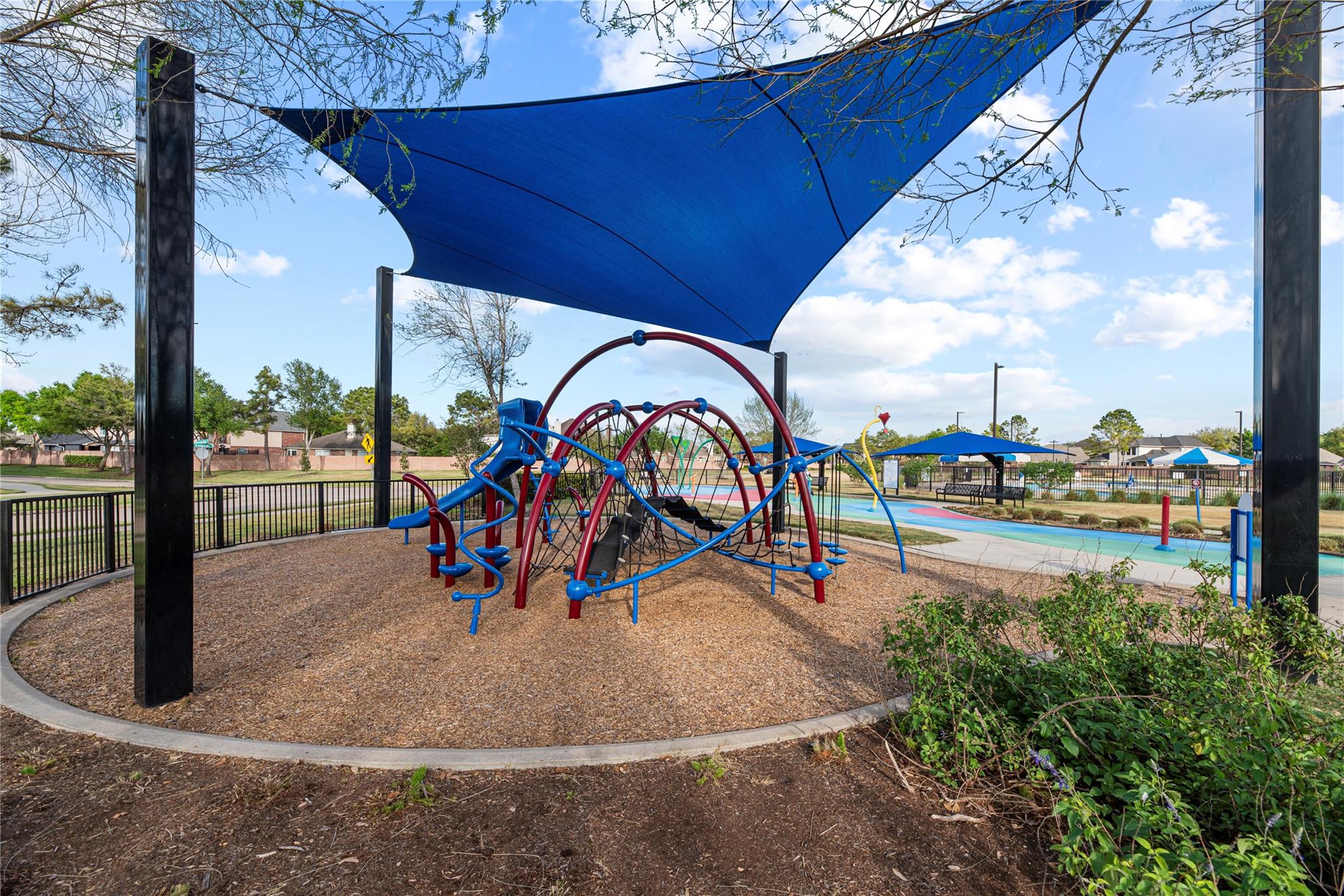 Neighborhood playground with a colorful climbing structure beneath a large blue shade sail.
