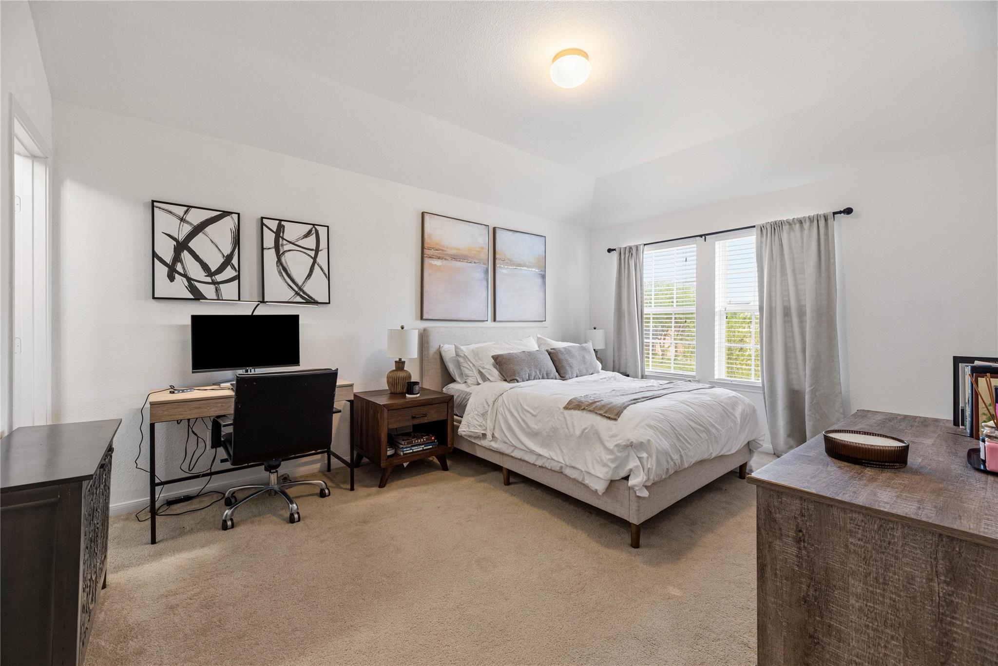 Staged bedroom with a white bed, large curtained windows, and a desk with a monitor.