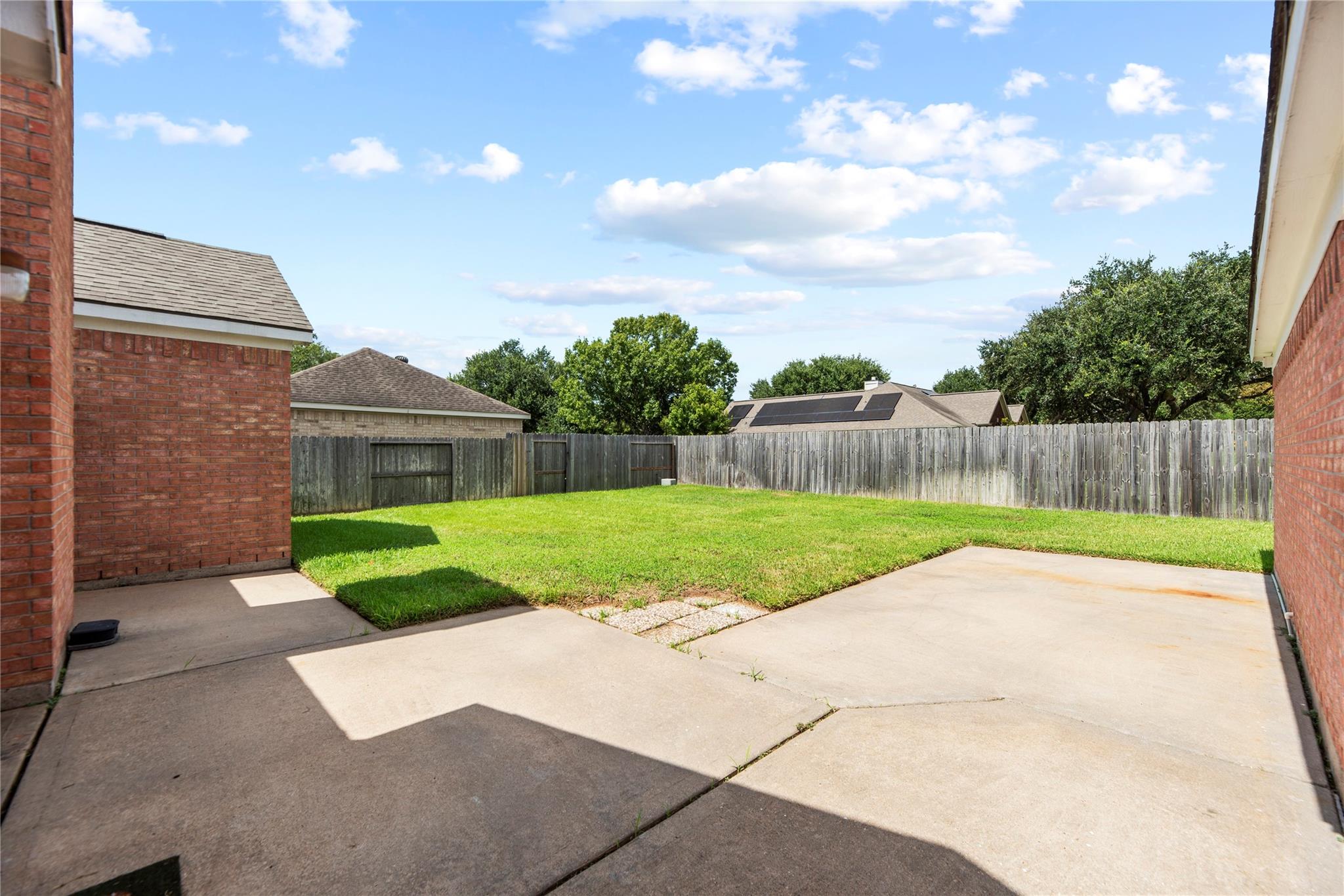 Fenced backyard with a large concrete patio and green lawn.