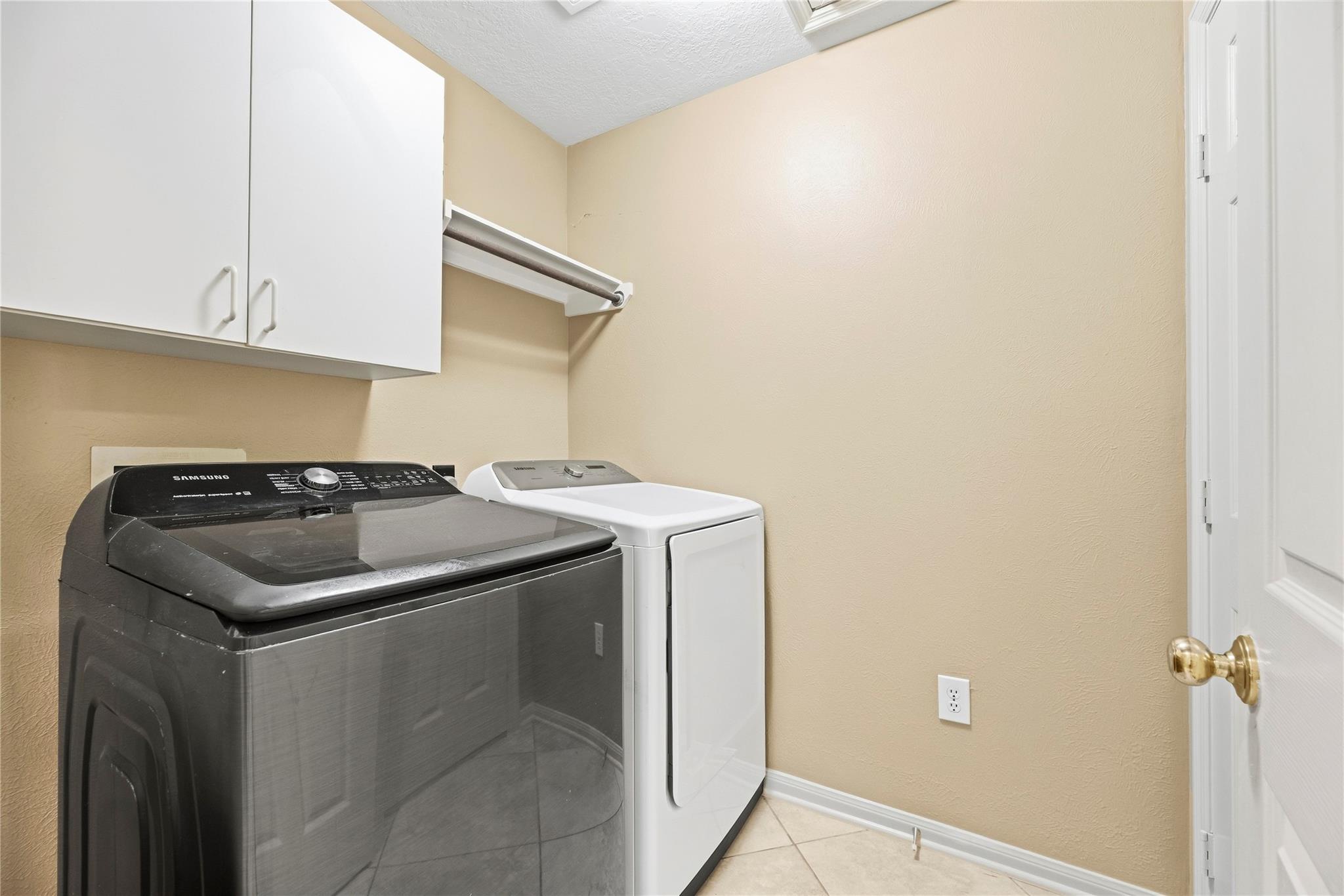 Laundry room with dark top-load washer, white dryer, and overhead storage cabinets.