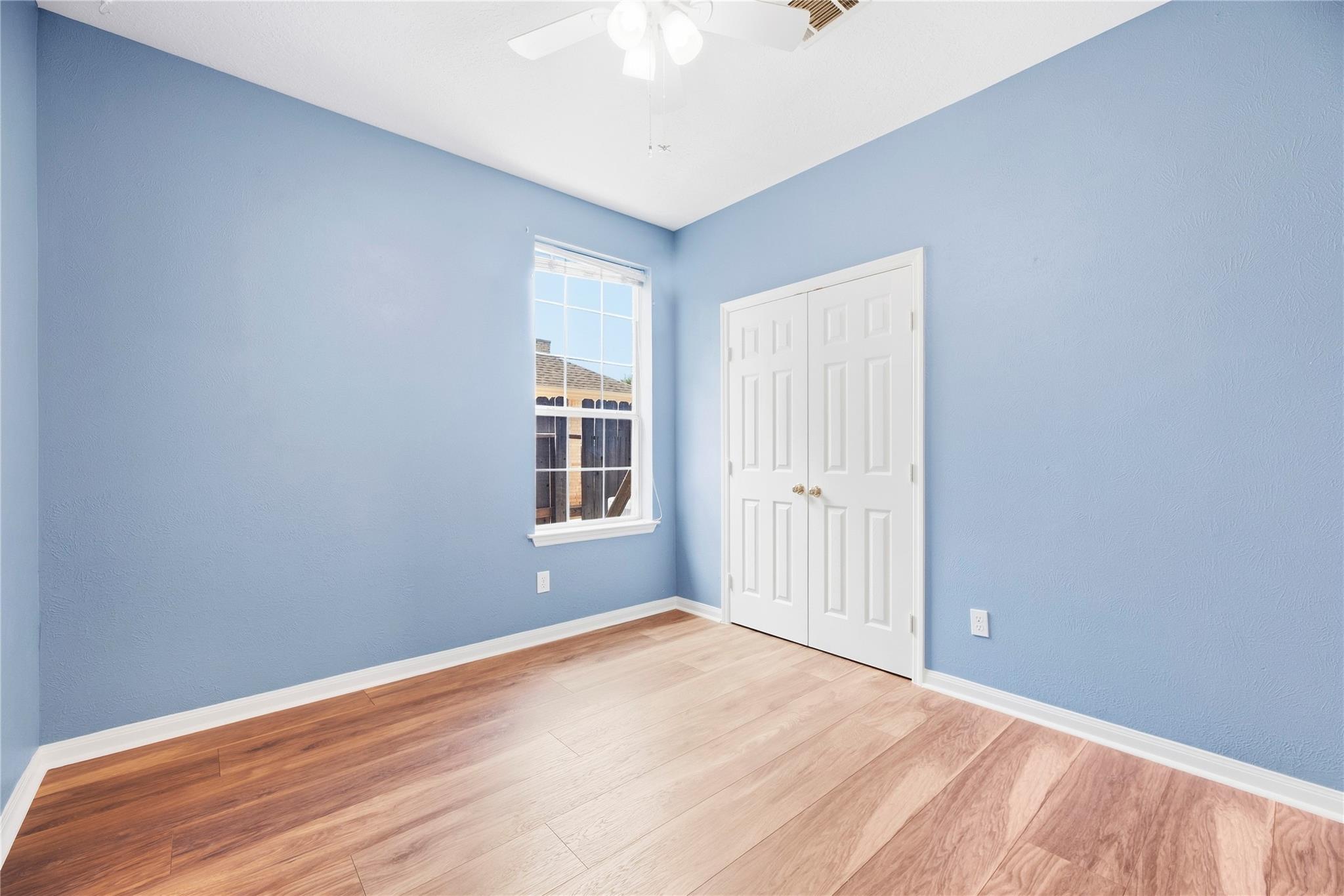 Empty blue bedroom with wood floors, a window, and double closet doors.