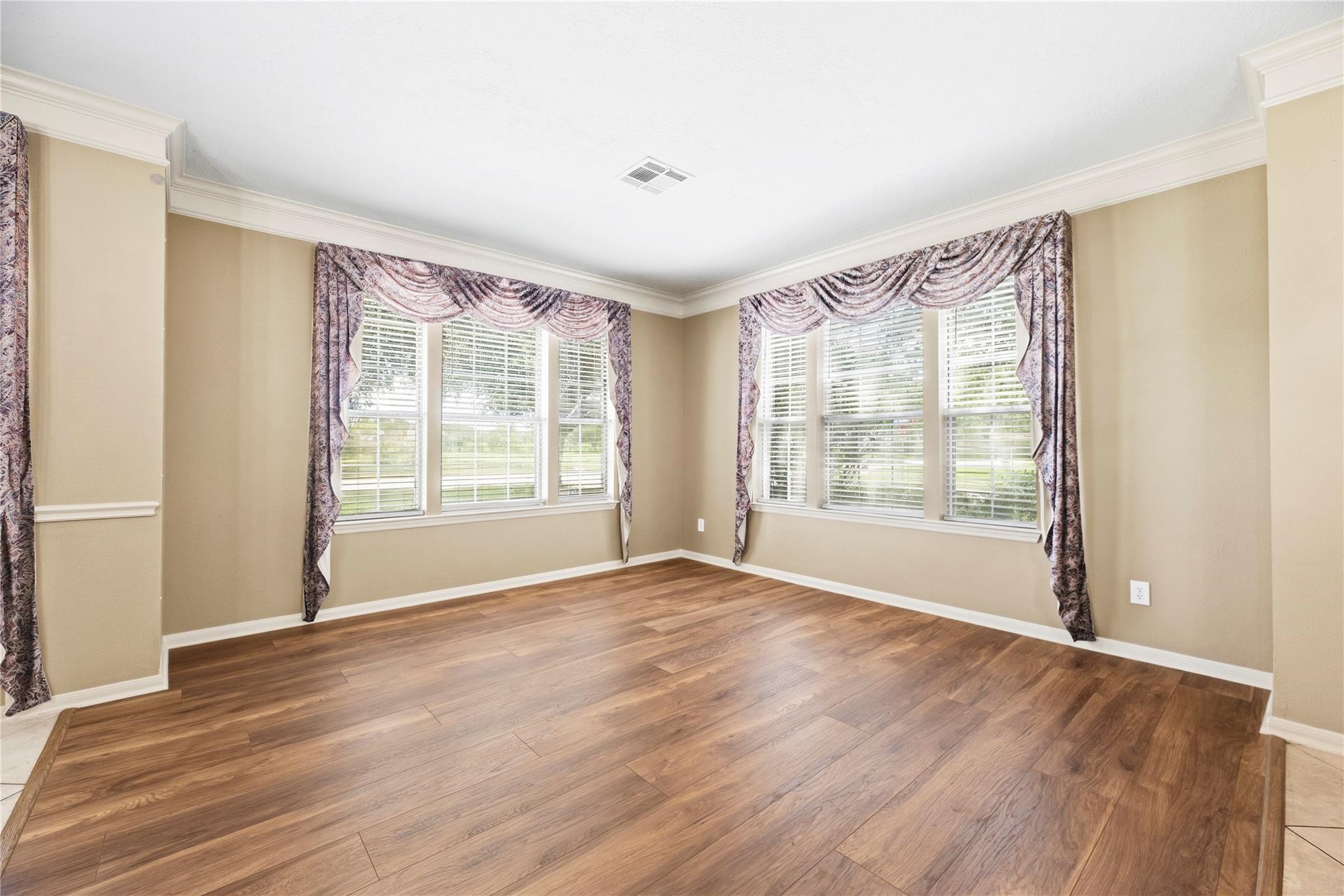 Empty room with wood-look flooring, beige walls, and two large curtained windows.