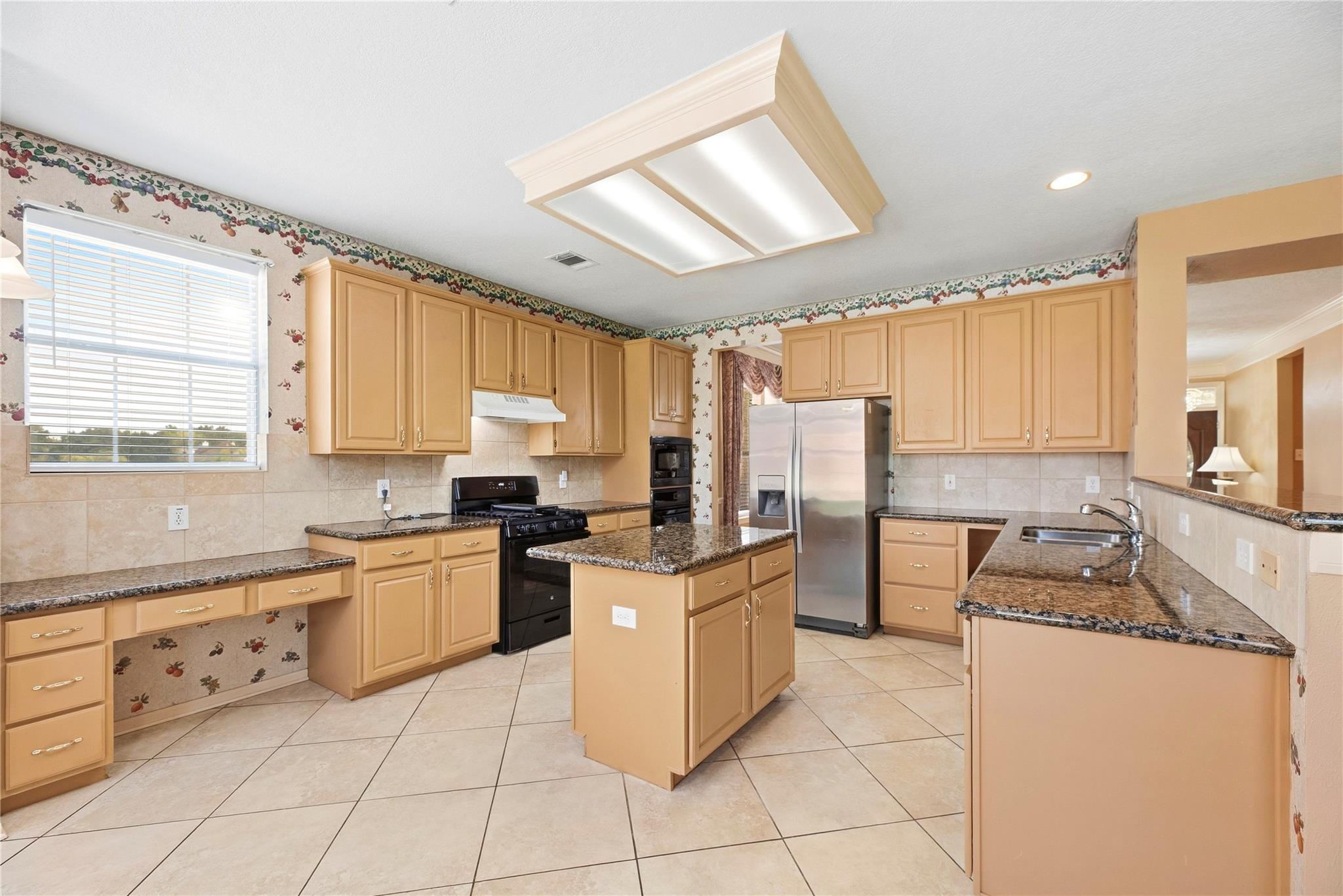 Kitchen with honey-colored cabinets, granite counters, central island, and stainless steel refrigerator.