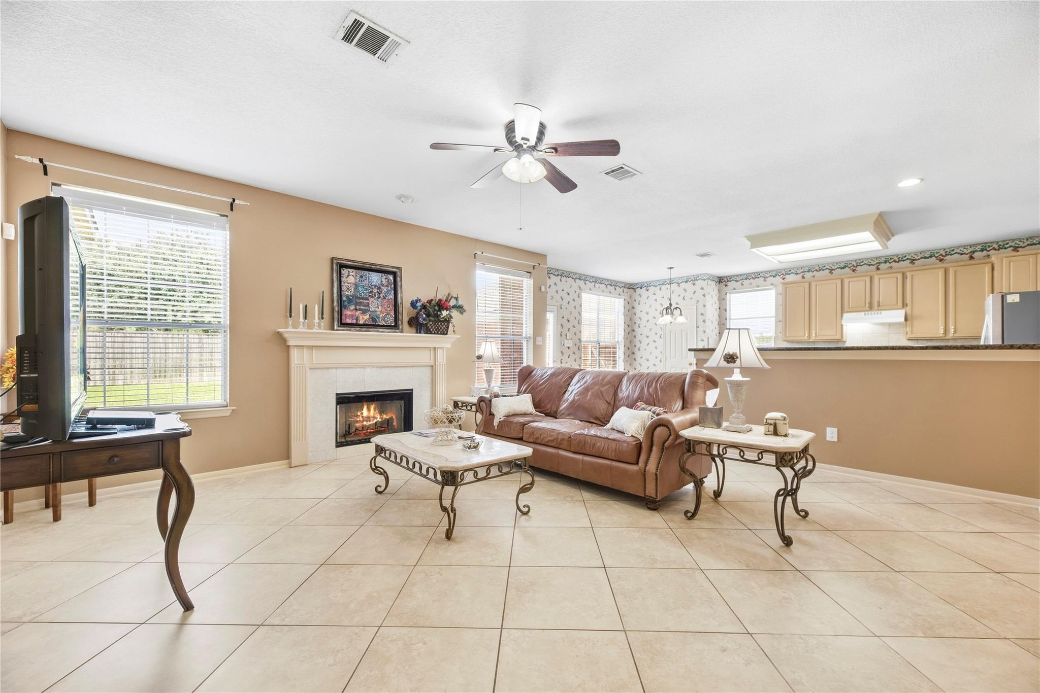 Living room with a brown leather sofa, tiled floor, fireplace, and open kitchen.