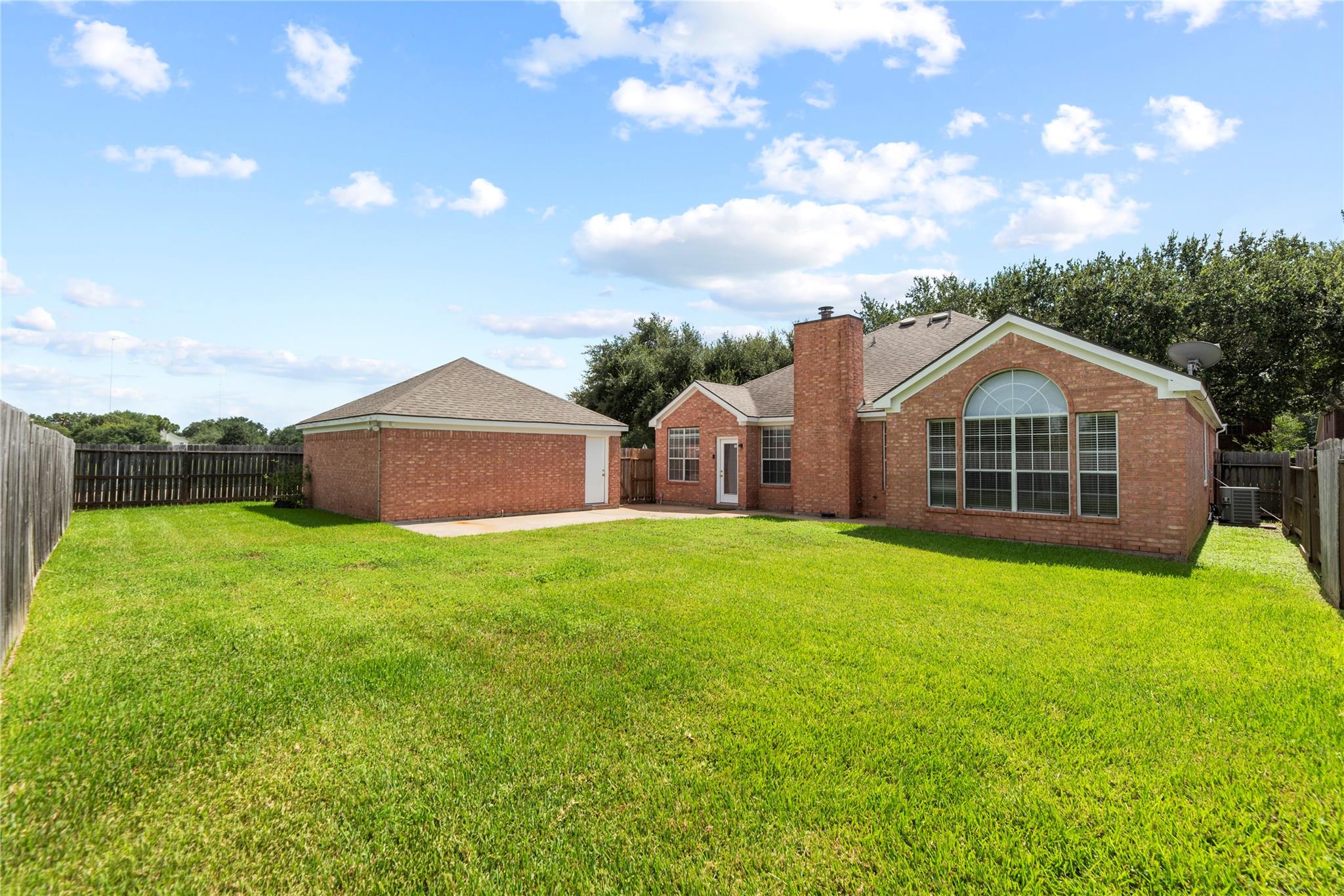Brick home with a large arched rear window and a spacious fenced backyard.