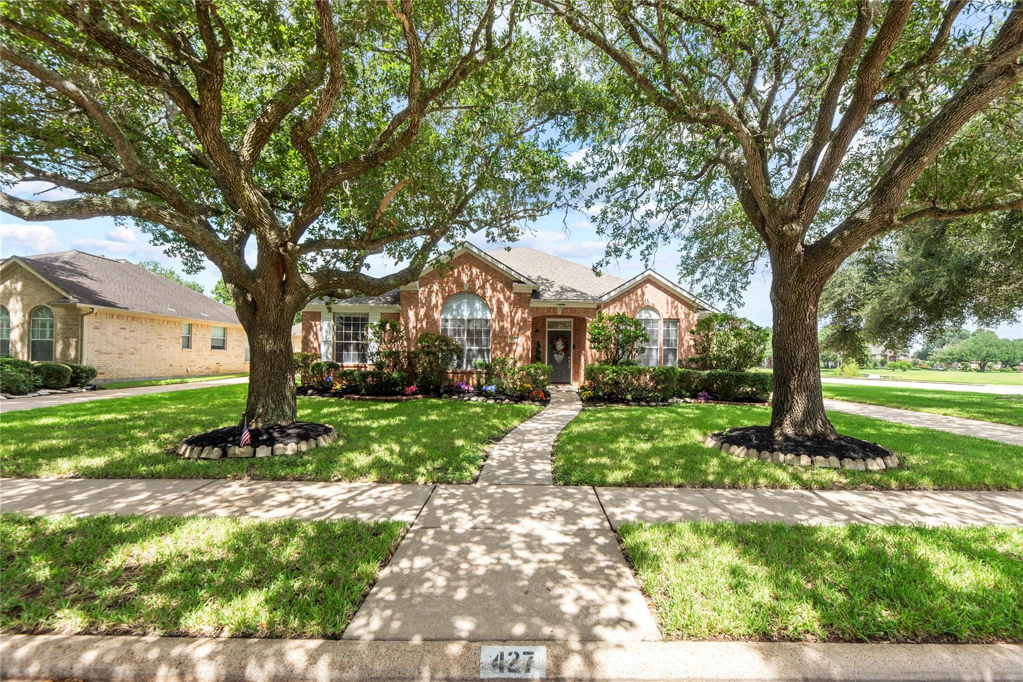 Brick house framed by two large shade trees, with a curved walkway to the front entrance.