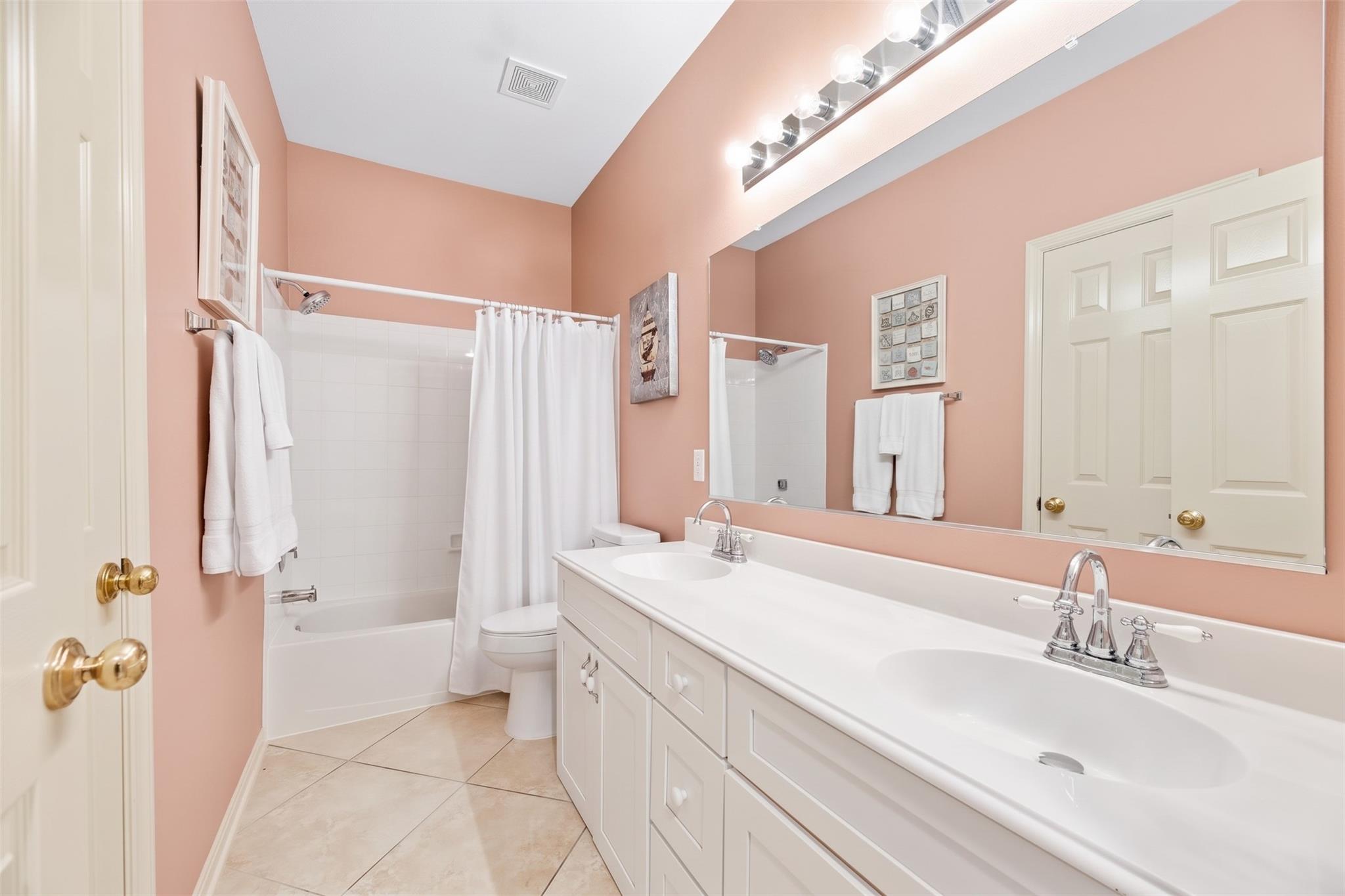 Bathroom with a white double-sink vanity, peach walls, and a tub-shower.