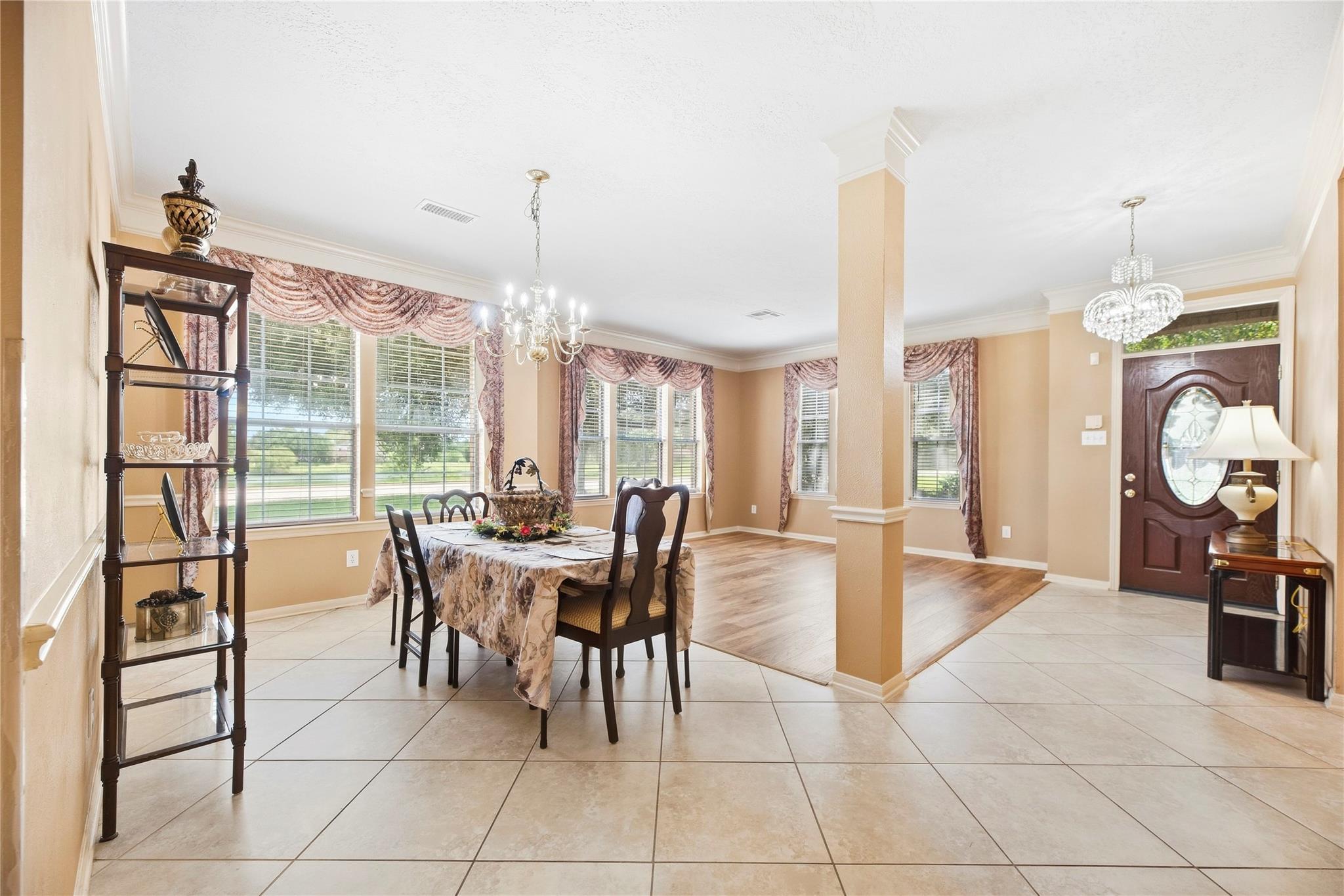 Dining room and entry foyer with a dark wood table, large windows, tiled floors, and an oval-glass front door.