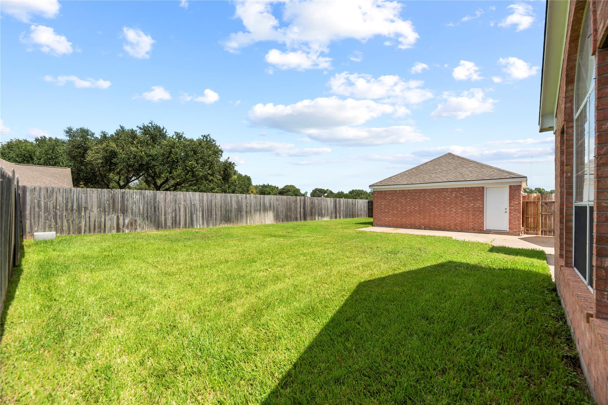 Fenced backyard with a broad green lawn and detached brick outbuilding beside the house.