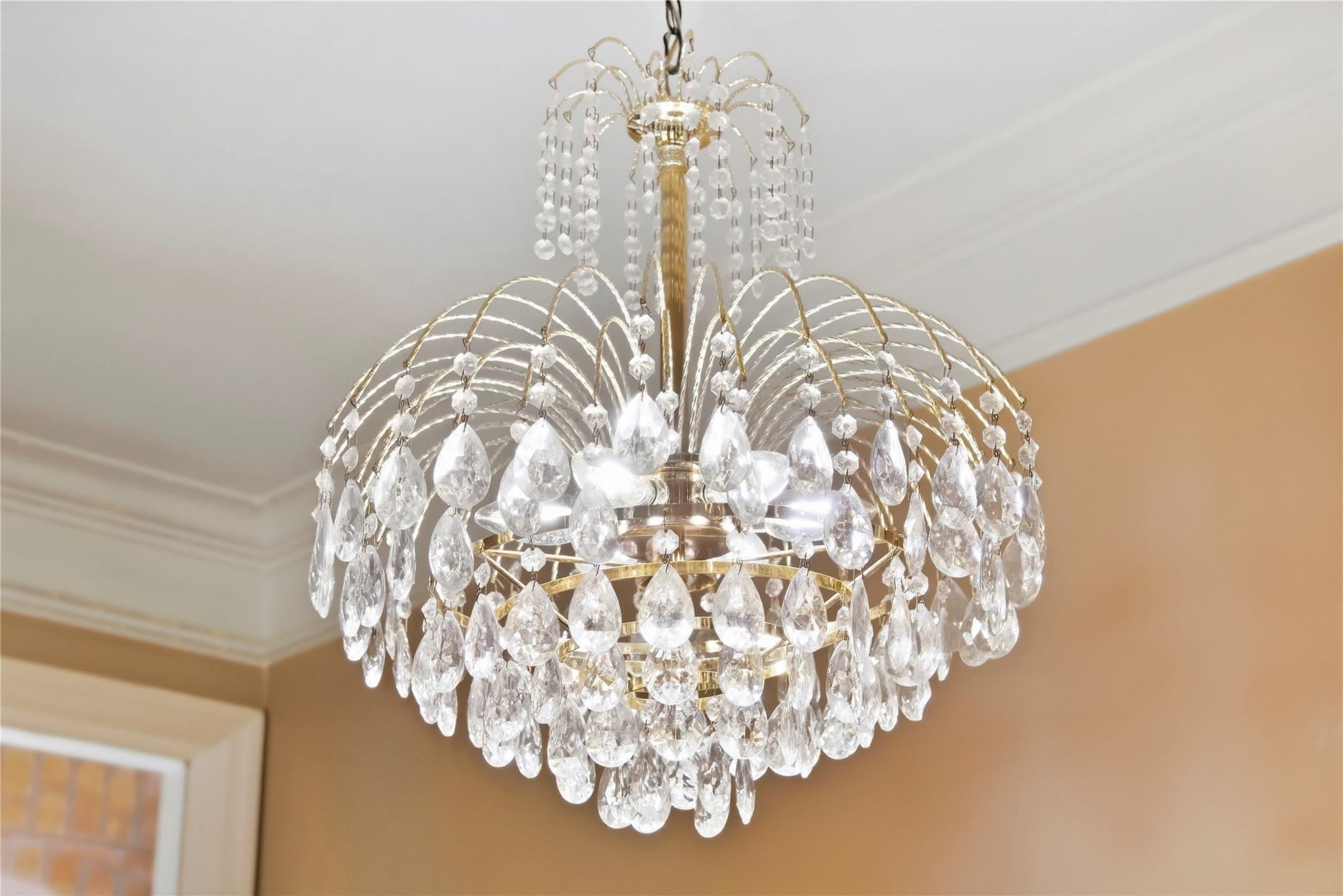 Crystal chandelier with gold-toned arms and hanging prisms beneath a white ceiling.