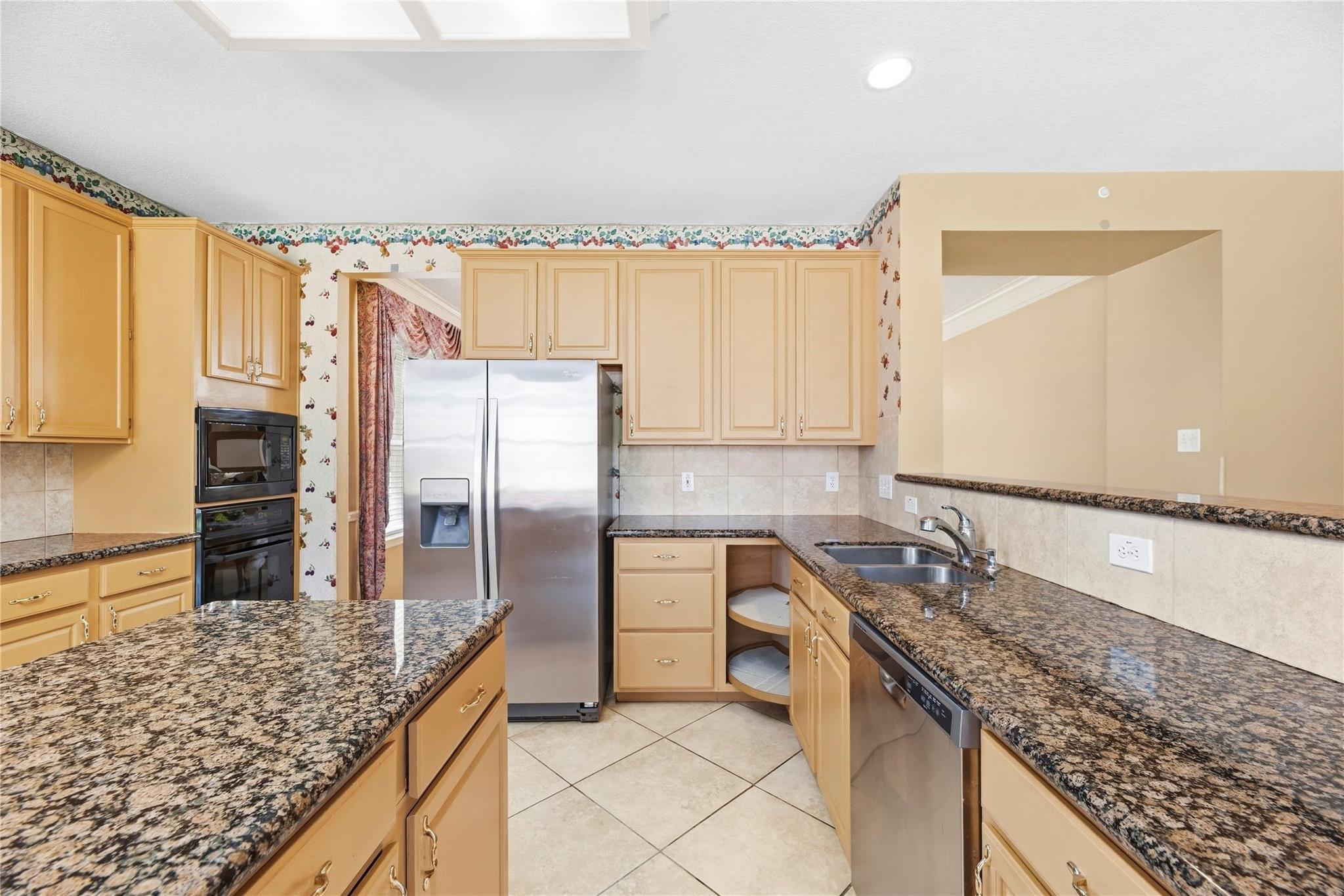 Kitchen with honey-colored cabinets, granite counters, stainless appliances, and floral wallpaper.