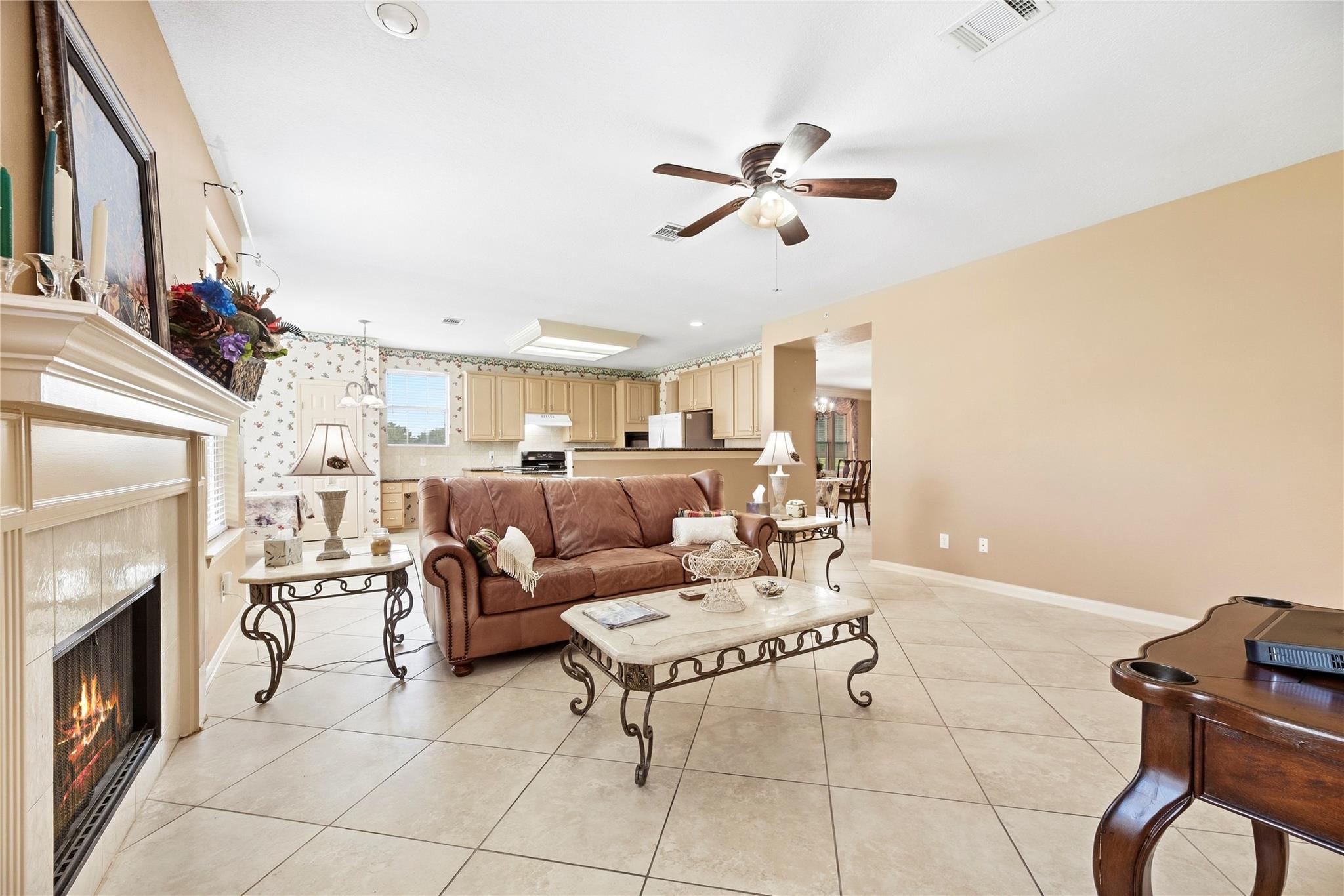 Living room with a brown leather sofa, tiled floors, fireplace, and open kitchen.