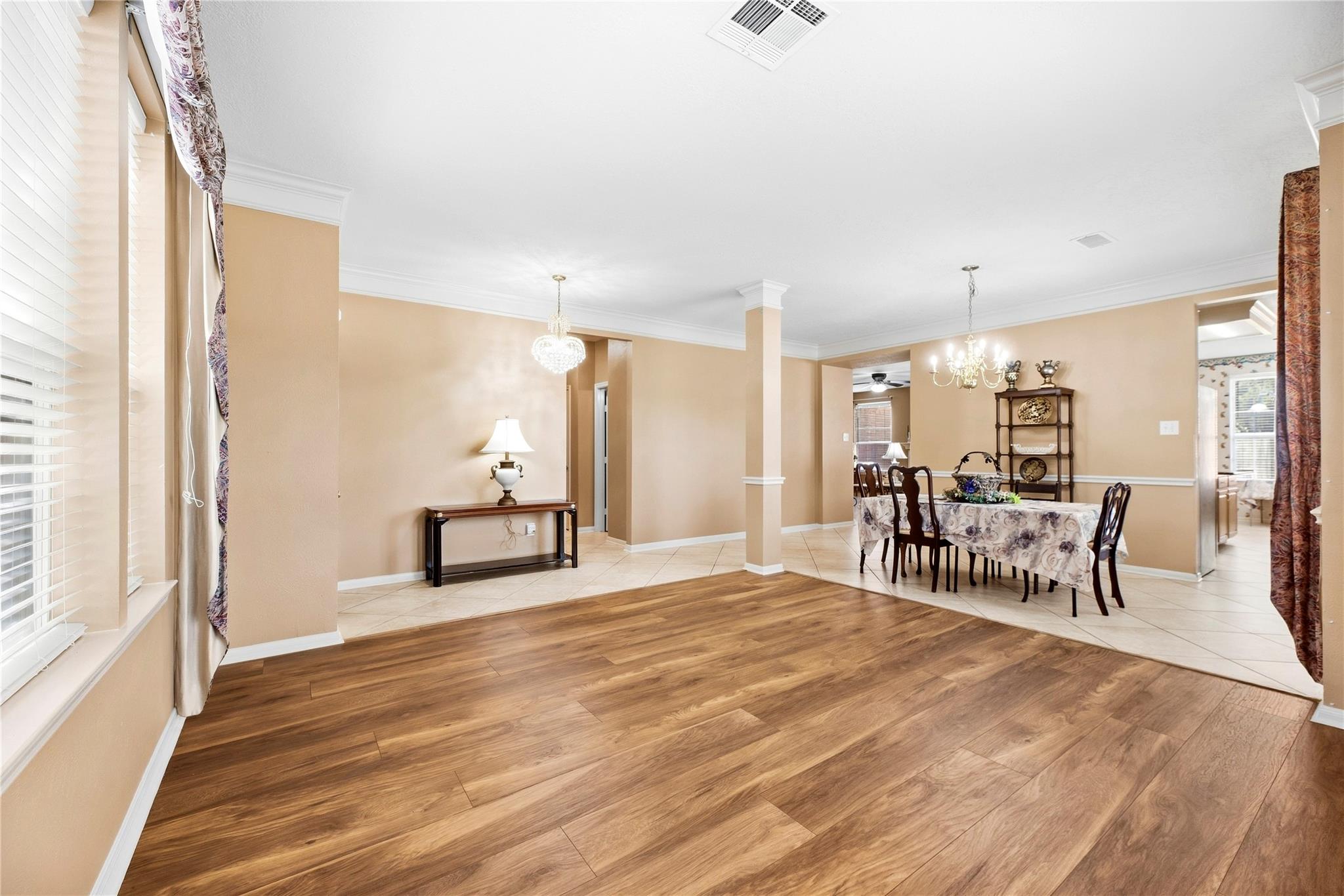 Open dining room with wood-look floors, beige walls, chandeliers, and a floral-covered table.