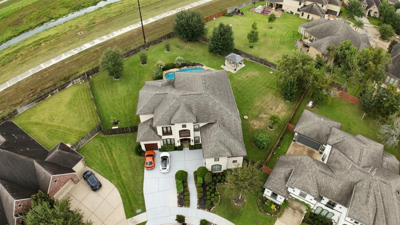 Aerial view of a two-story home with a fenced lawn, swimming pool, gazebo, and landscaped driveway.