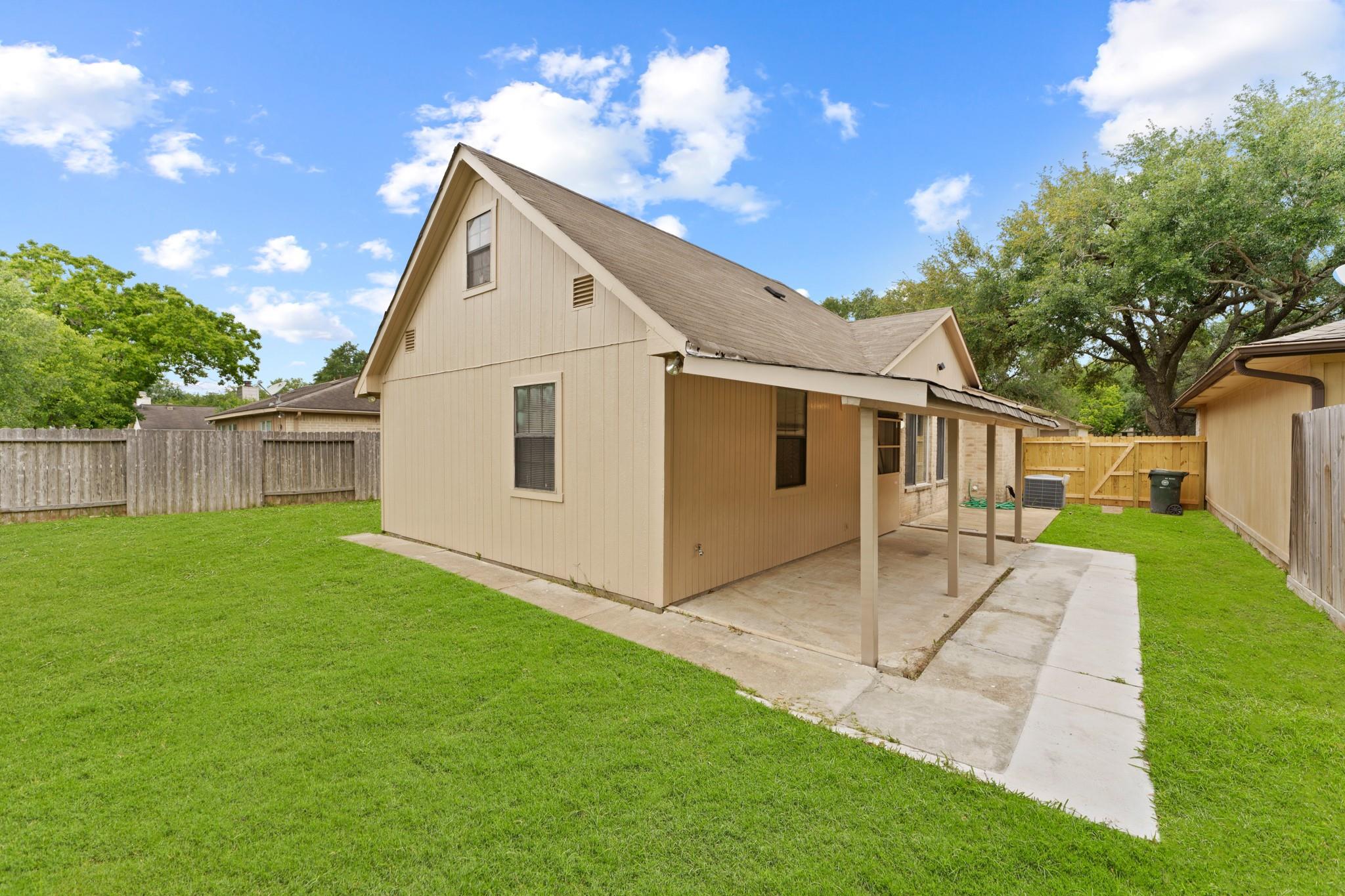 Home’s rear exterior with a covered patio, fenced lawn, and concrete walkway.