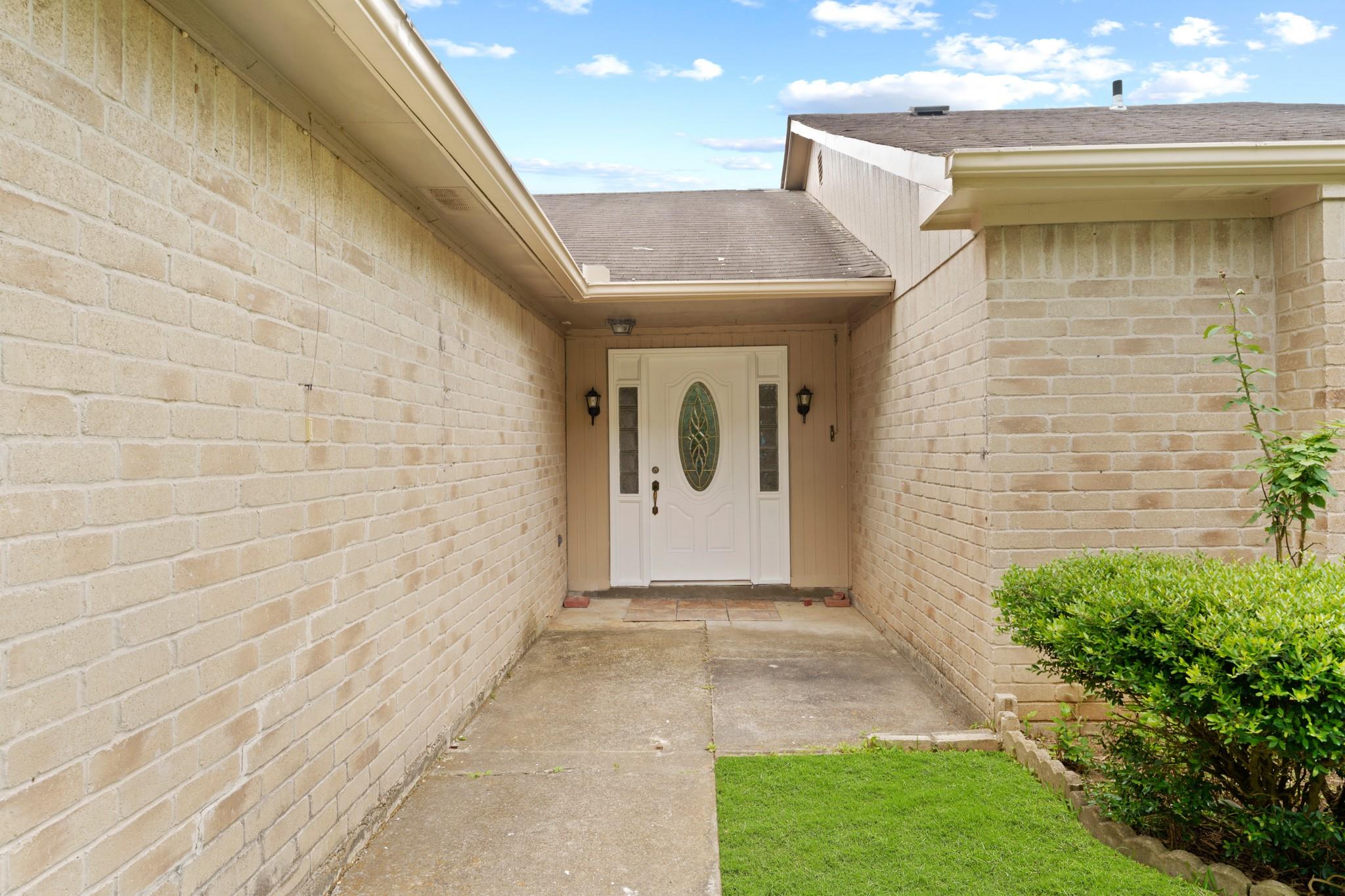 Brick home entry with a covered walkway leading to a white decorative glass front door.