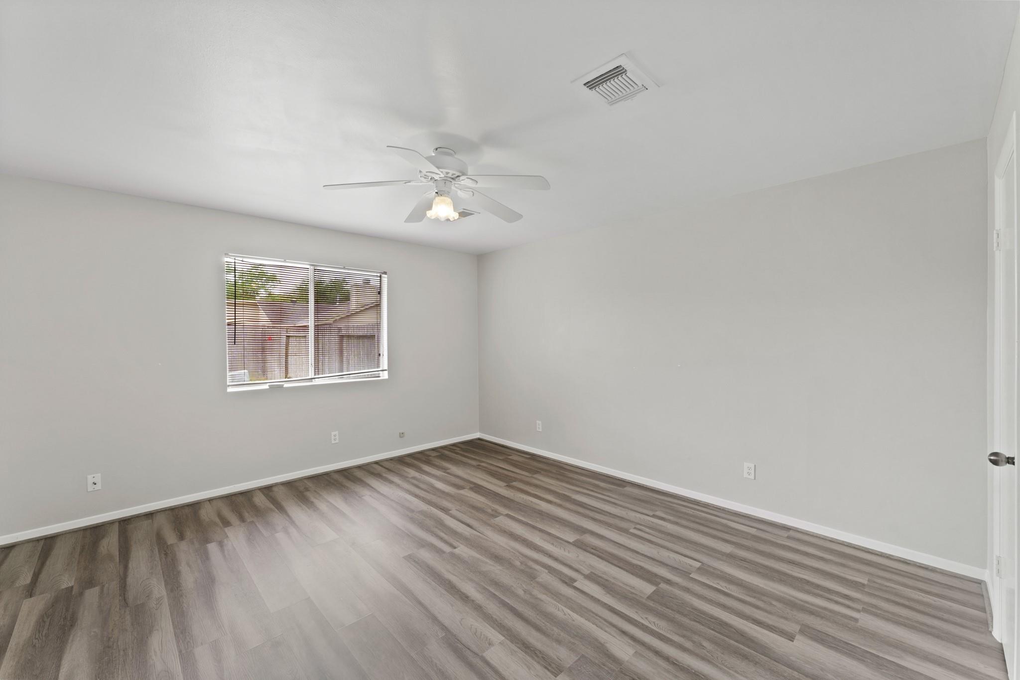 Empty bedroom with gray-brown plank flooring, a ceiling fan, and a window with blinds.