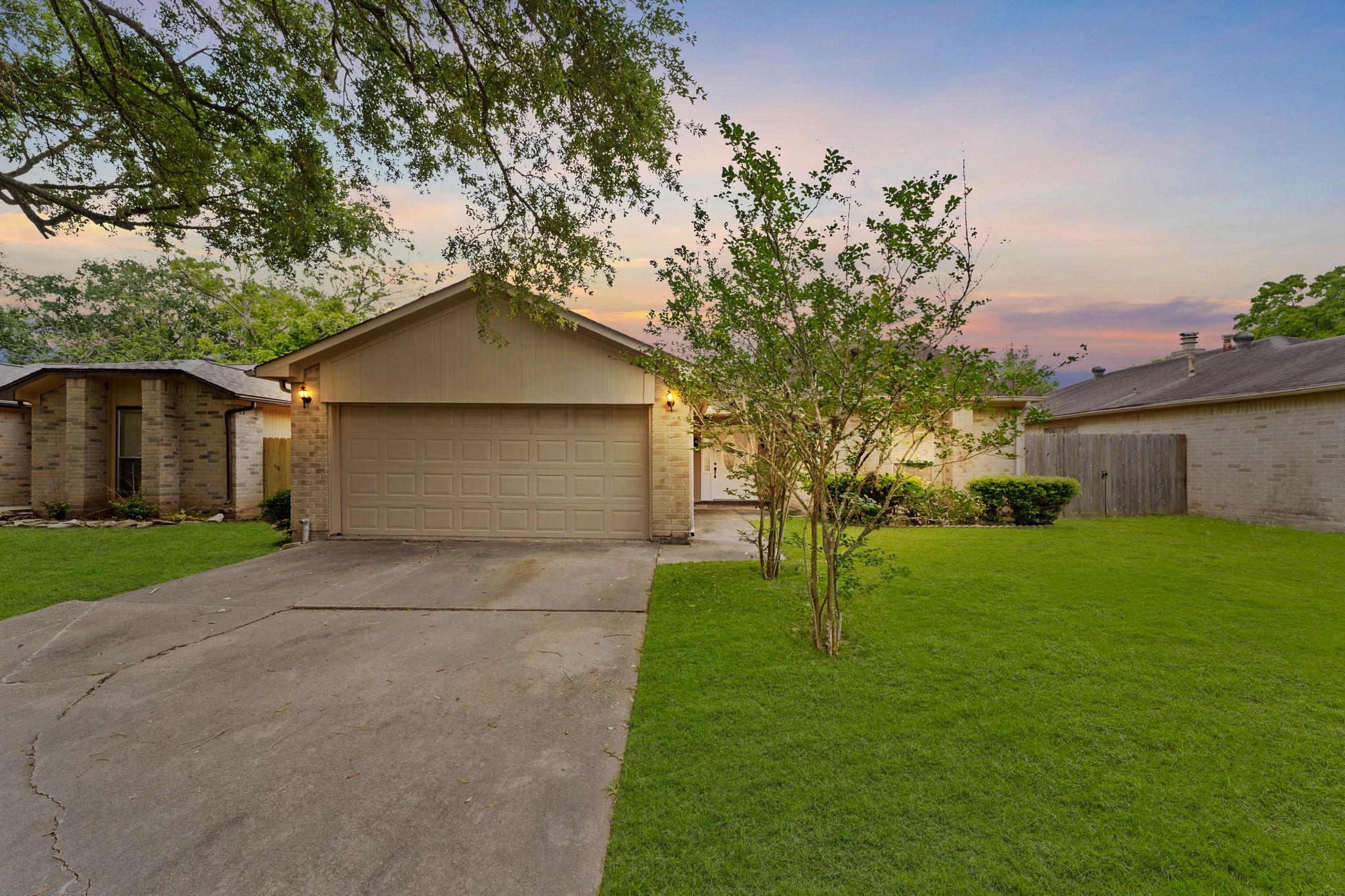 Brick home with a double garage, broad driveway, and green lawn at dusk.