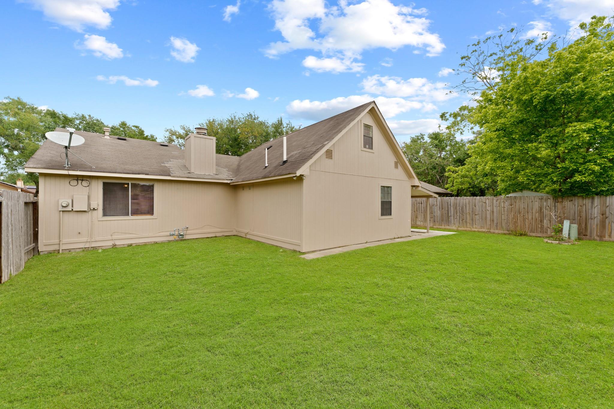 Rear of a beige two-story home with a broad lawn and fenced backyard.
