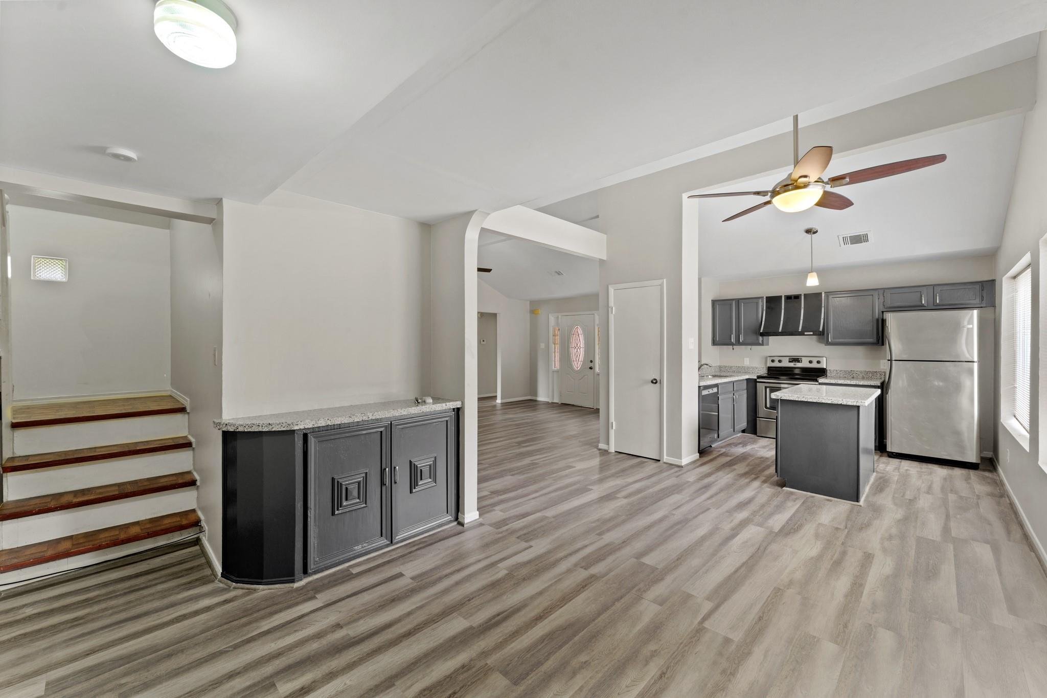 Vacant open-plan kitchen with gray cabinets, stainless steel appliances, granite counters, and stairs.