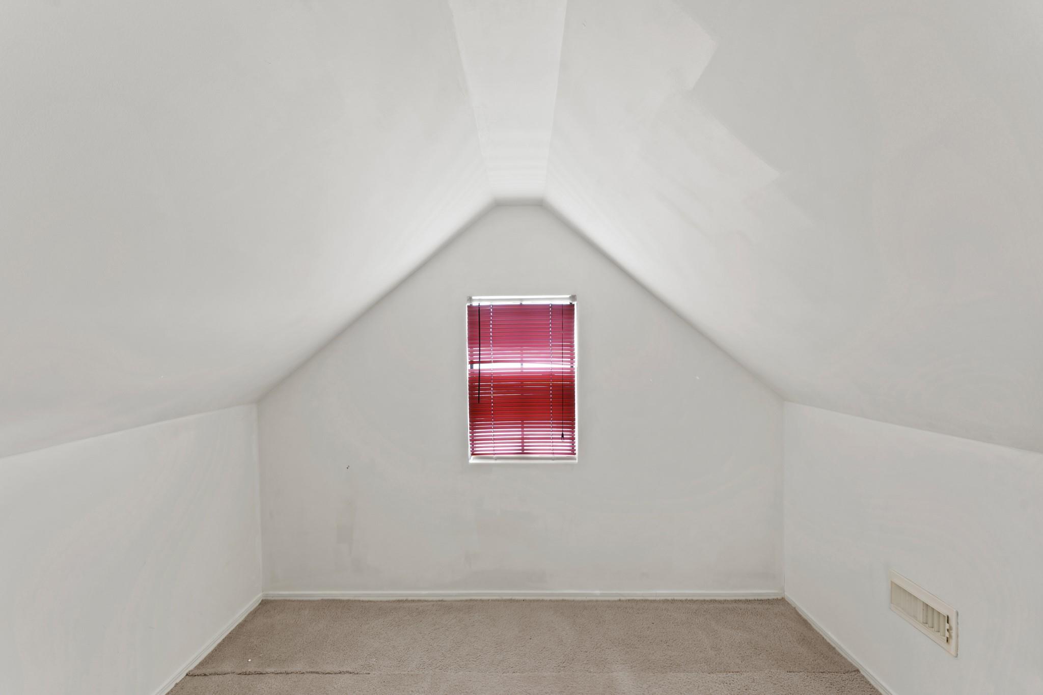 Empty carpeted room with sloped ceilings and a small window with red blinds.