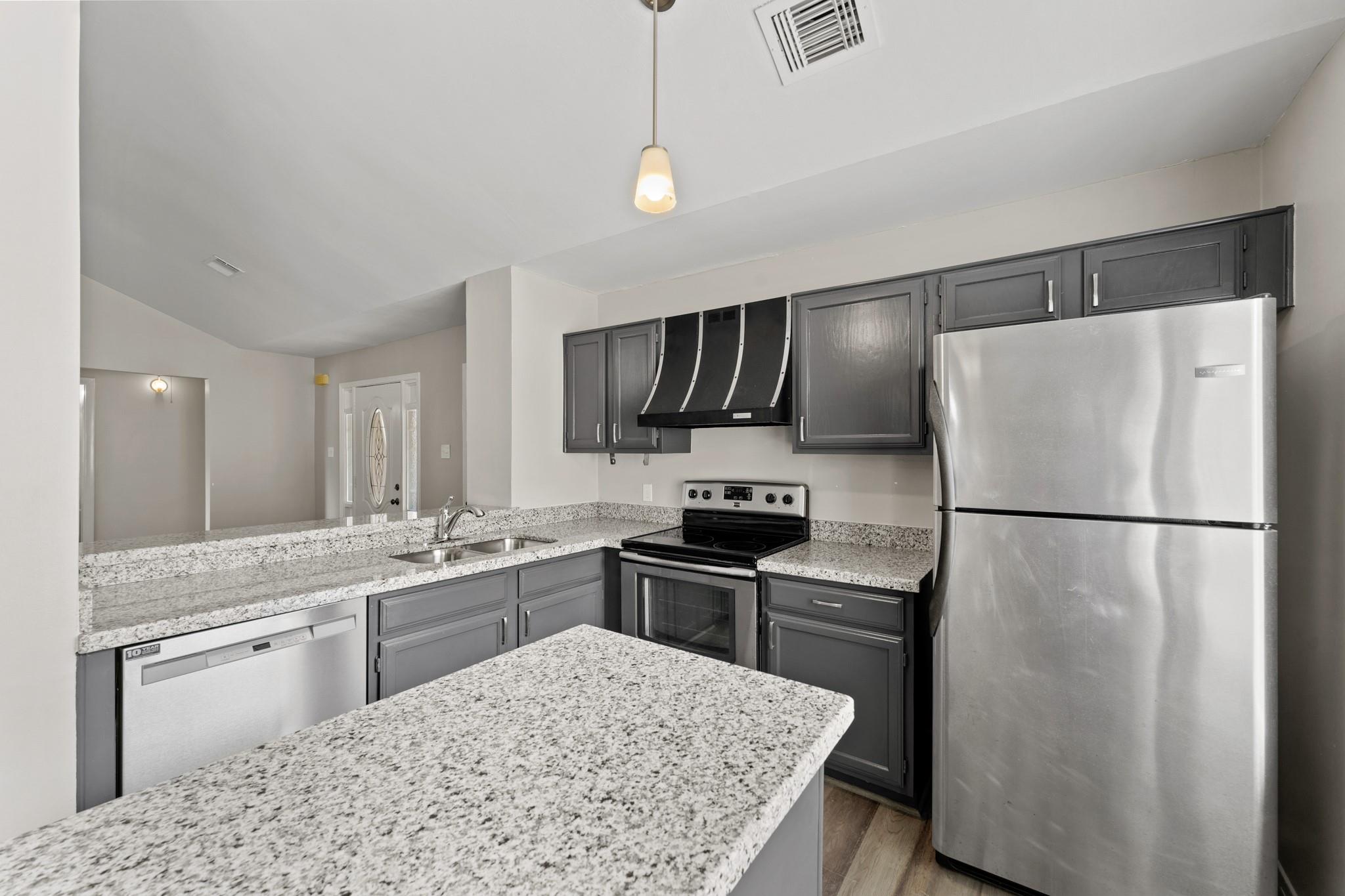 Kitchen with gray cabinets, granite counters and island, and stainless steel appliances.