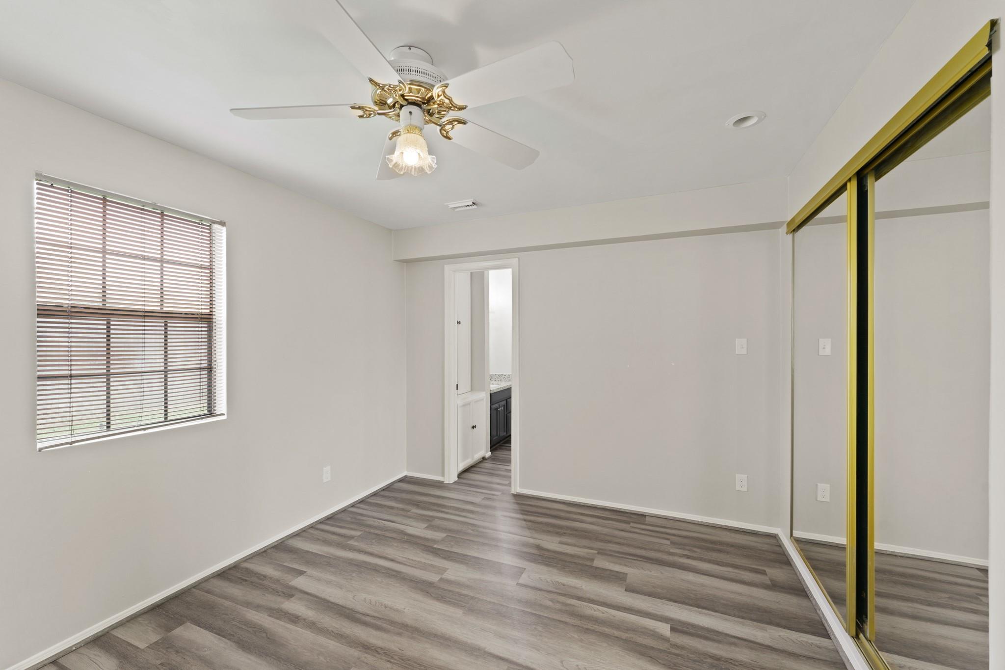 Empty bedroom with gray wood-look flooring, mirrored closet doors, and a ceiling fan.