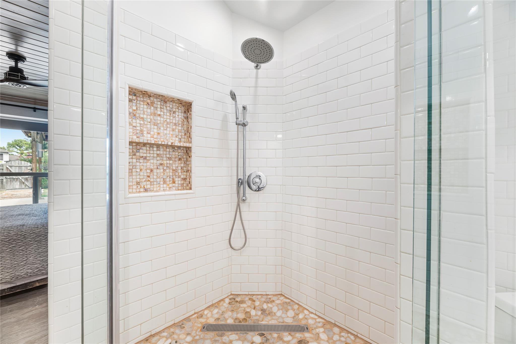 Walk-in shower with white subway tile, pebble floor, and recessed mosaic-tile niche.