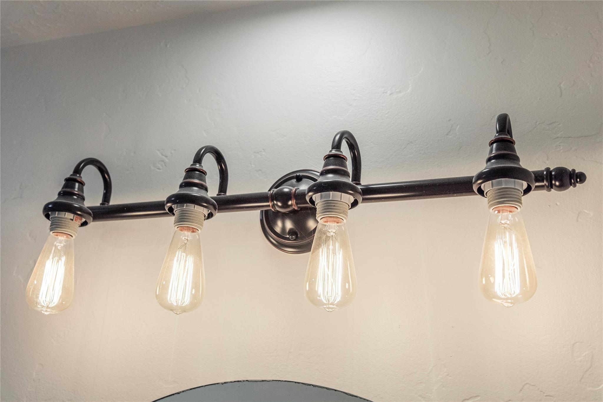 Four-bulb dark metal vanity light with exposed glowing bulbs above a mirror.