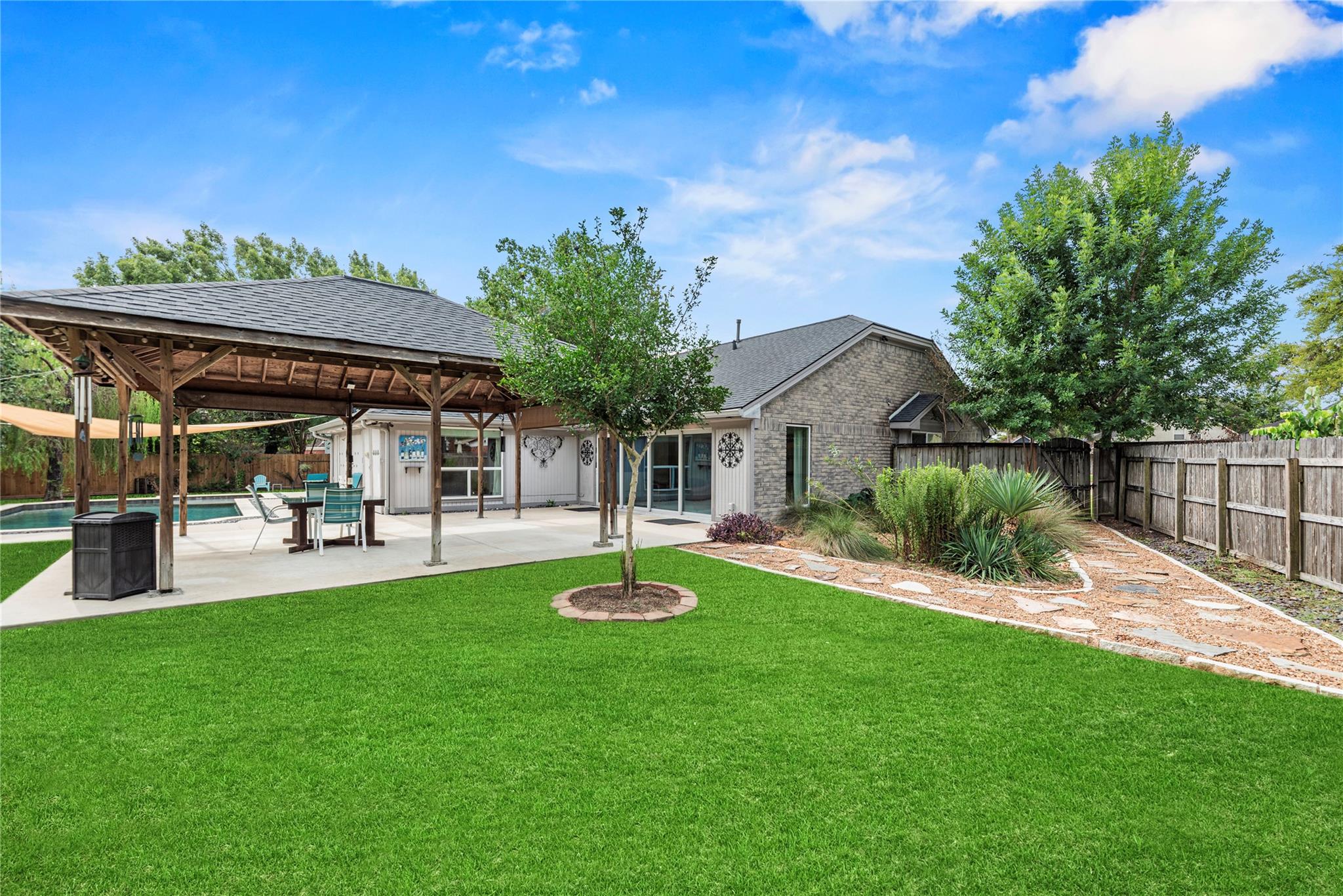 Backyard with a covered patio, swimming pool, landscaped beds, and a wide green lawn.