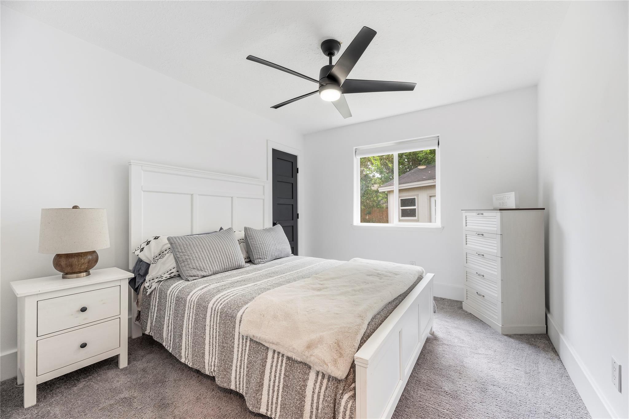 Furnished bedroom with striped bedding, a black ceiling fan, and a window overlooking trees.