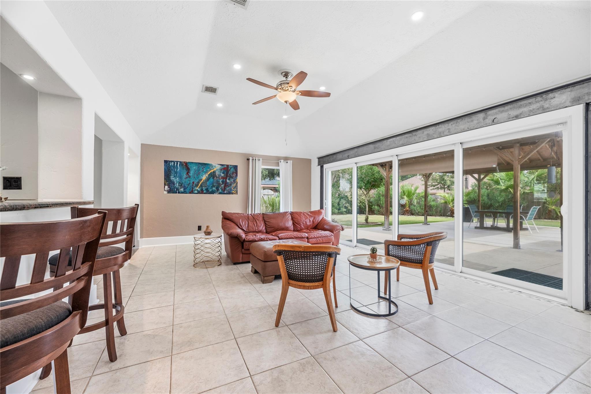 Living room with leather sofa and large sliding doors opening to a covered patio and leafy backyard.