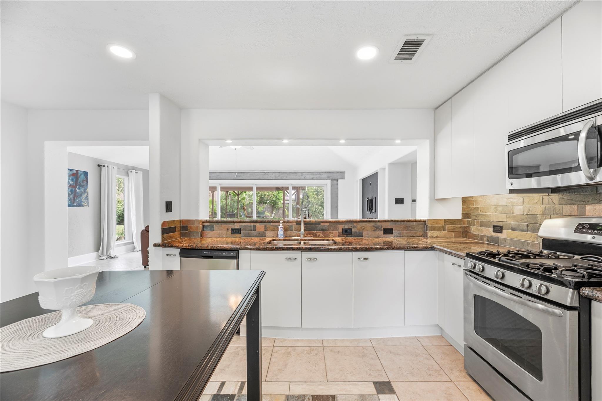 Kitchen with white cabinets, stainless steel appliances, warm stone counters, and a view toward the backyard.