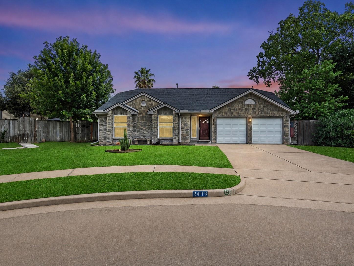 Single-story stone-faced home with a two-car garage, broad driveway, and lawn at dusk.
