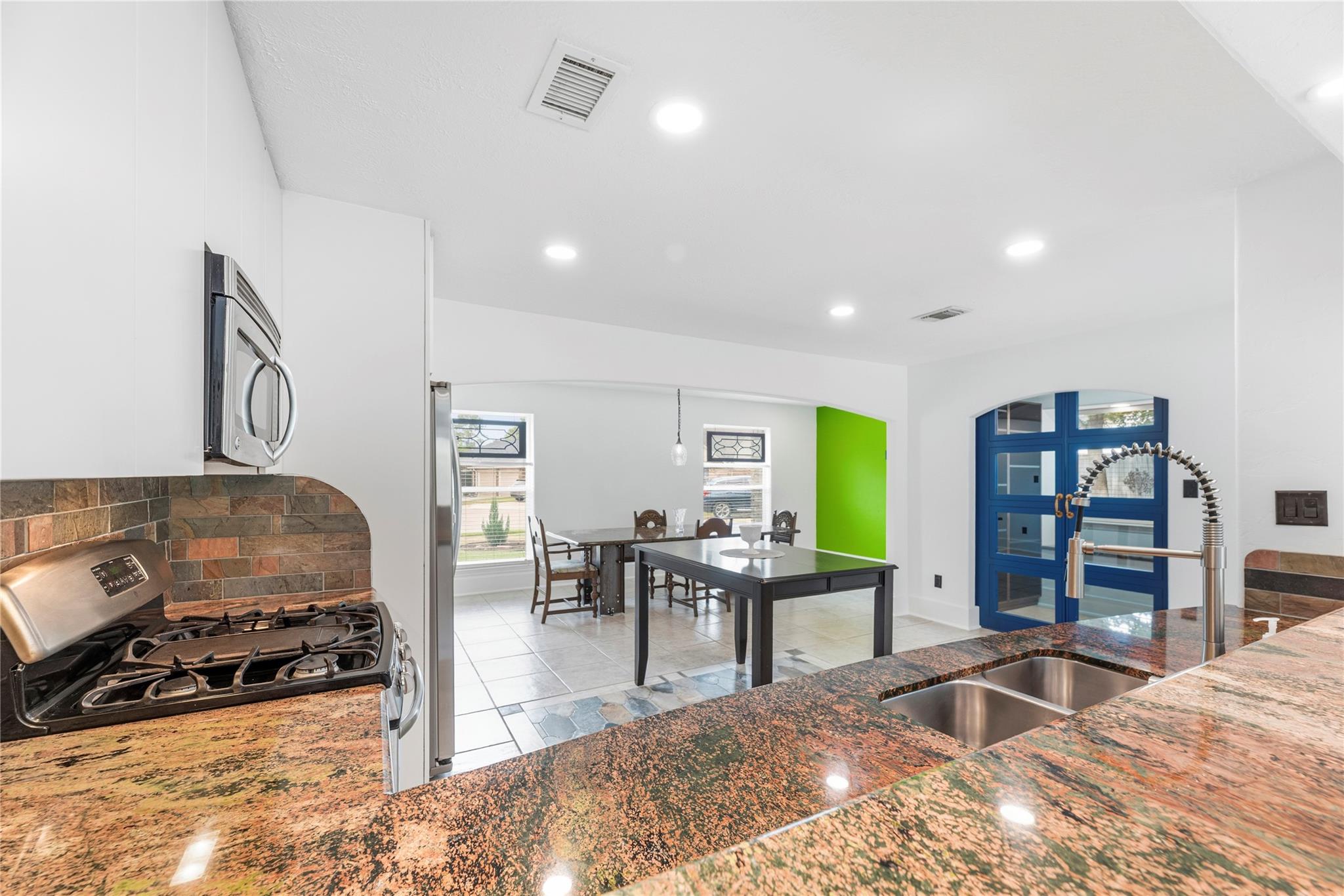 Kitchen with granite counters, stainless steel appliances, and a dining area with blue-framed windows.