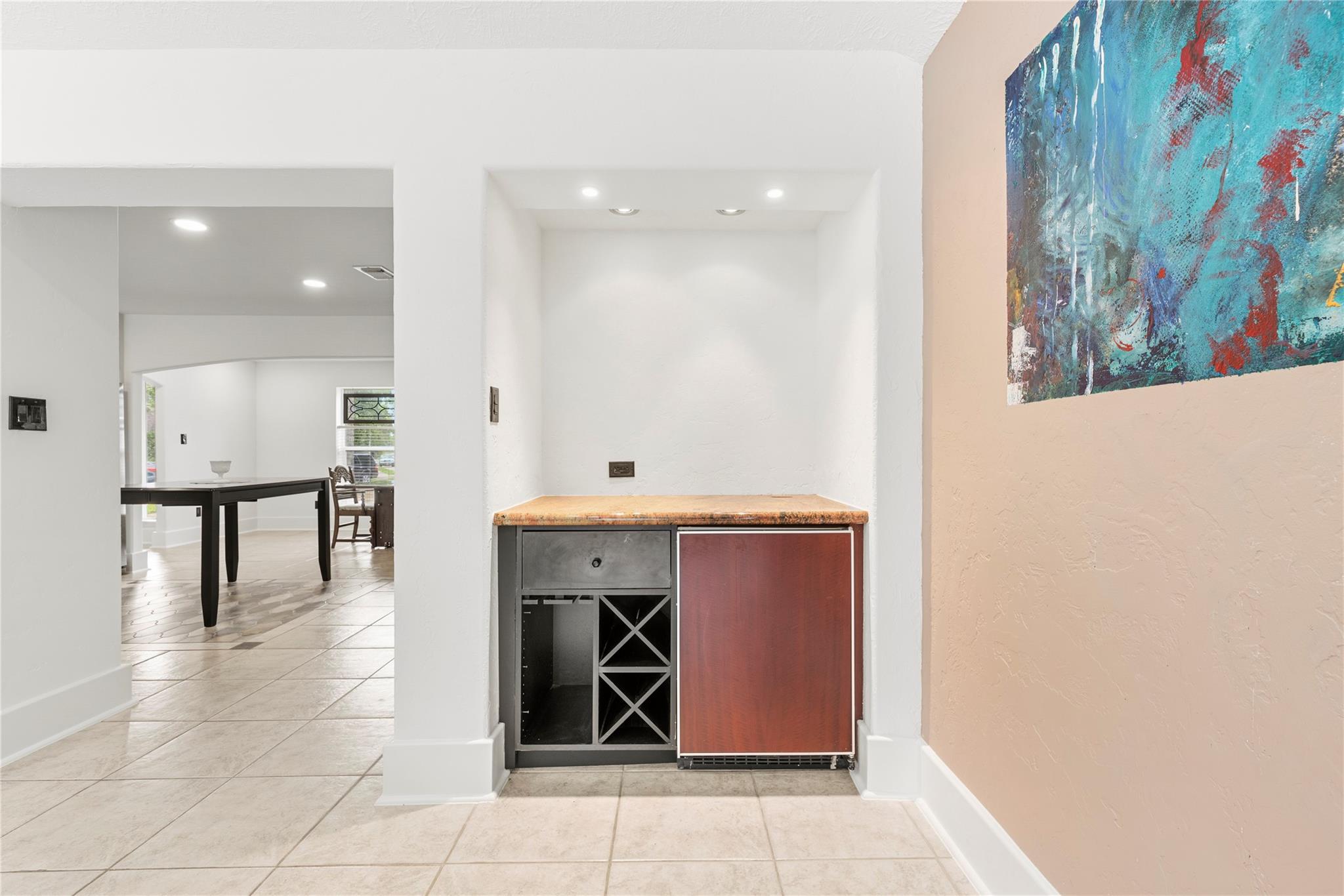 Built-in wine nook with stone counter, wine storage, and beverage refrigerator beside a dining area.