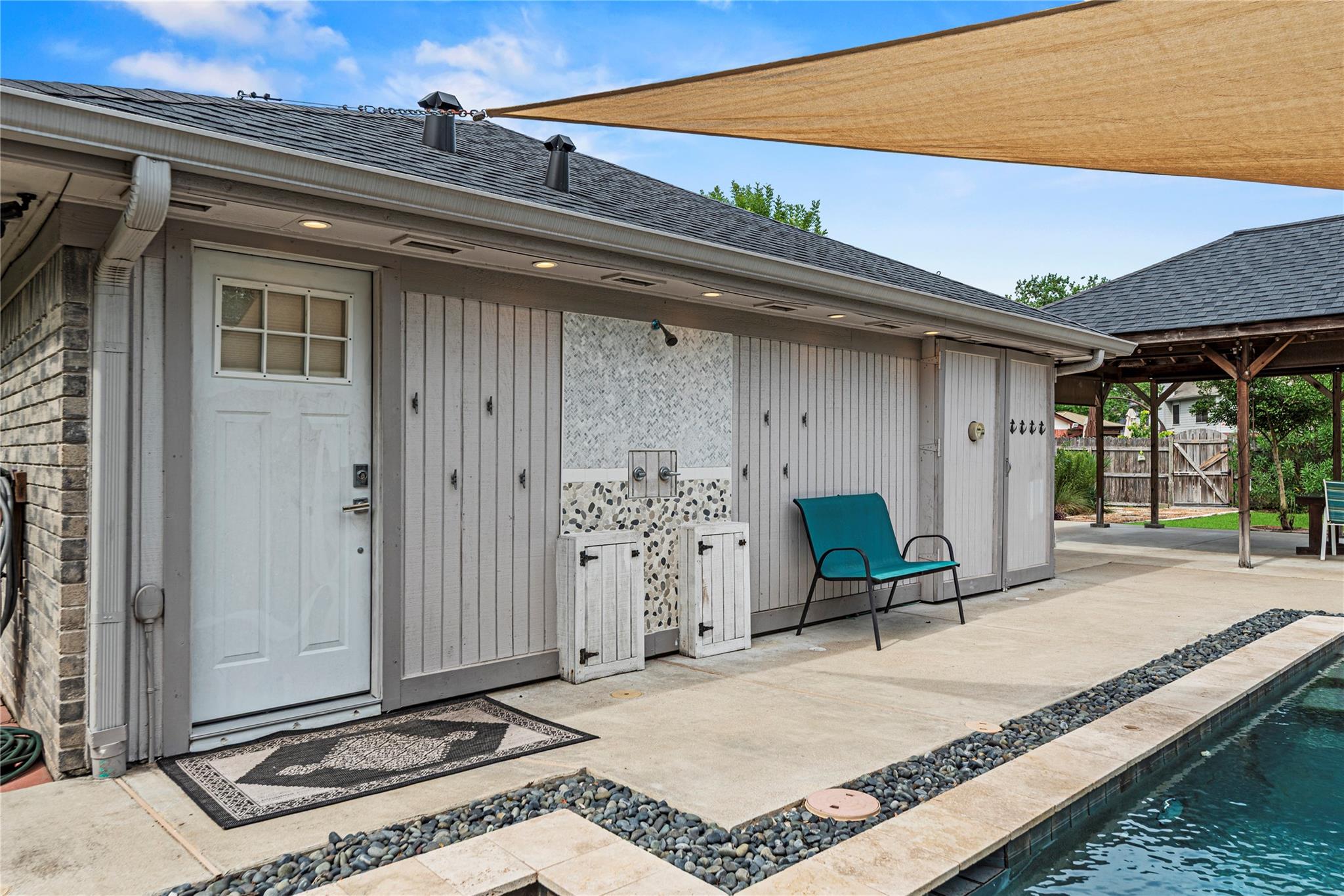 Backyard pool beside a gray pool house with an outdoor shower and teal bench.