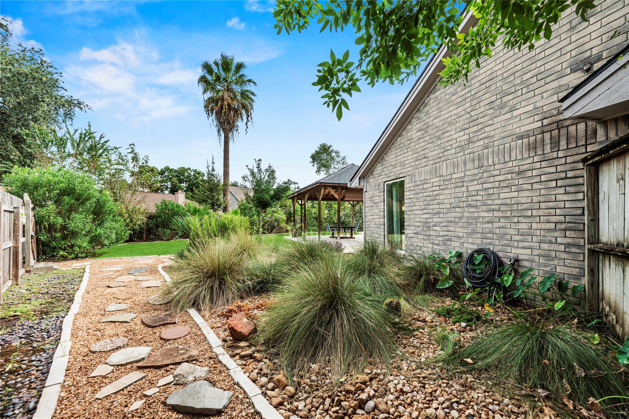 Landscaped backyard with a stepping-stone path and covered pergola beside a brick house.