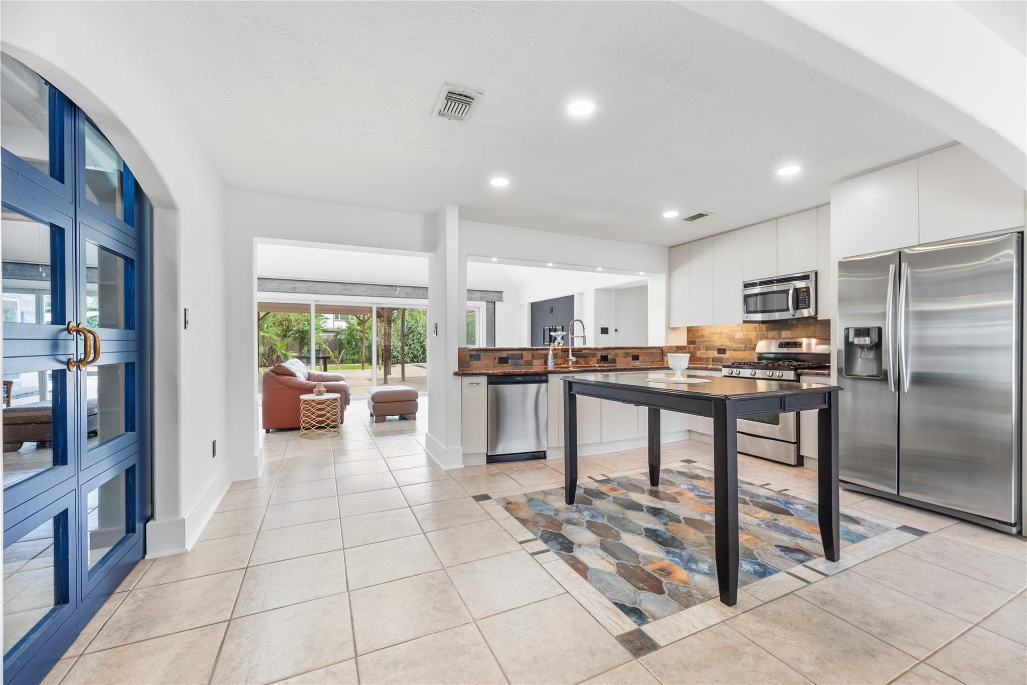 Open kitchen with white cabinets, stainless appliances, dark island, and blue-framed glass doors beside the living area.