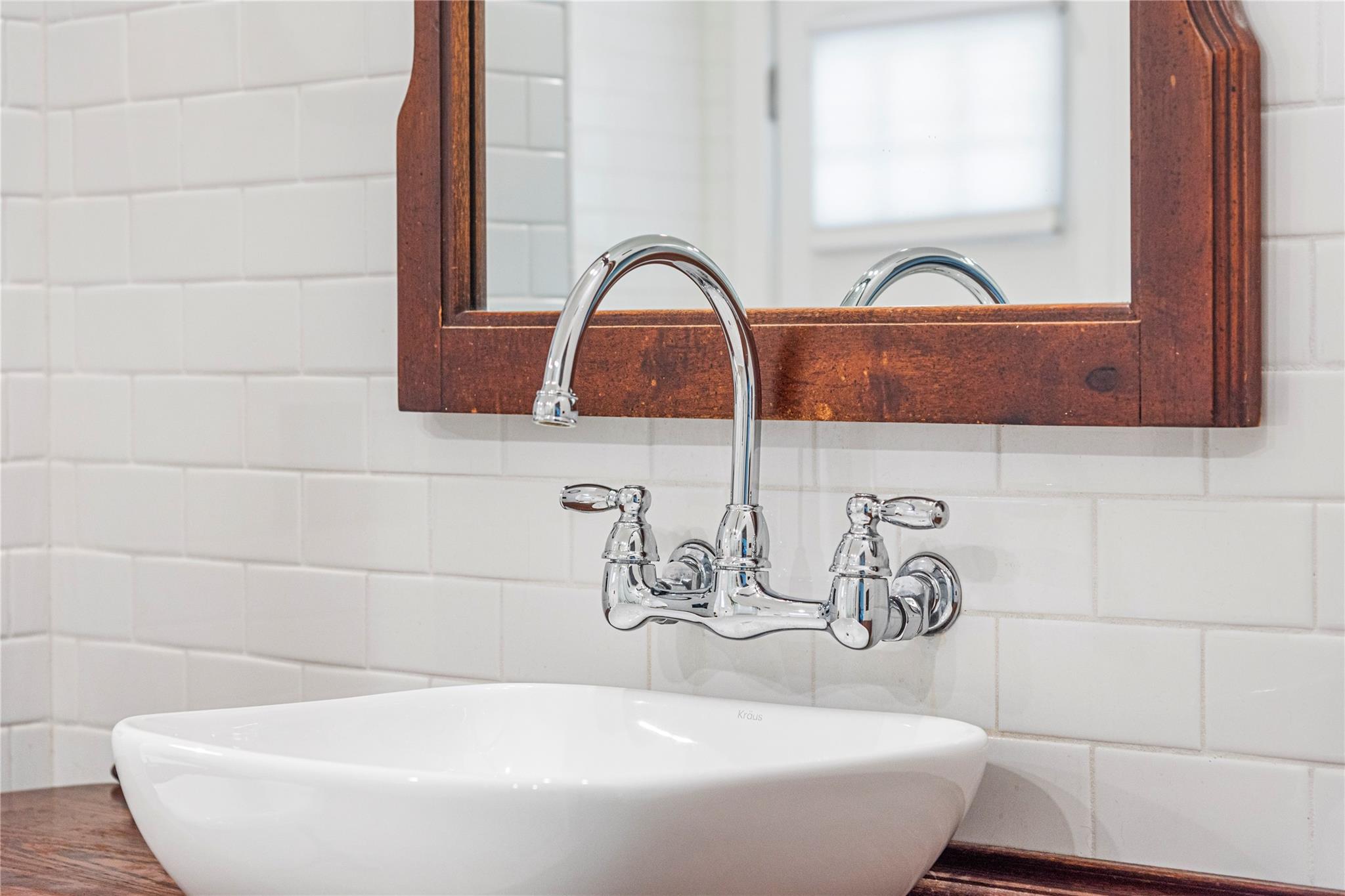 White vessel sink with a chrome wall-mounted faucet beneath a dark wood-framed mirror.