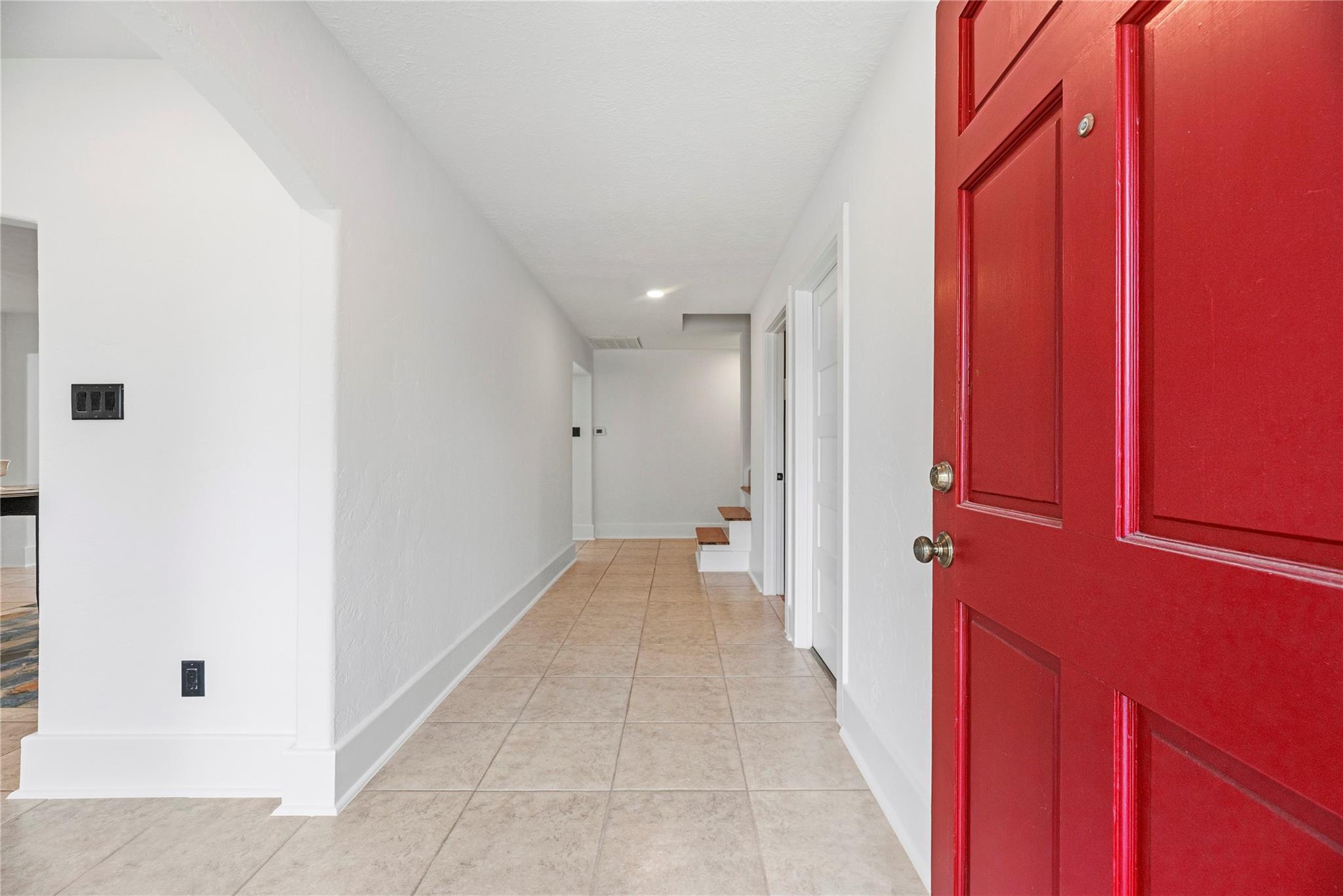 Entry hall with beige tile flooring and a bright red front door.