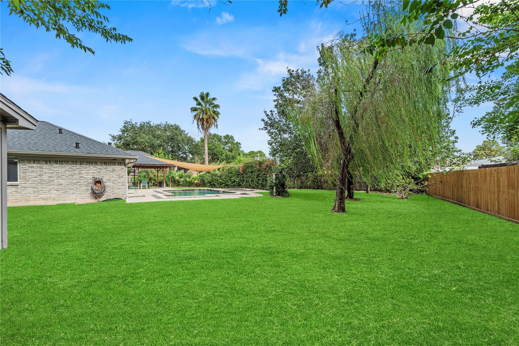 Backyard with a large lawn, swimming pool, shade sail, and mature trees.