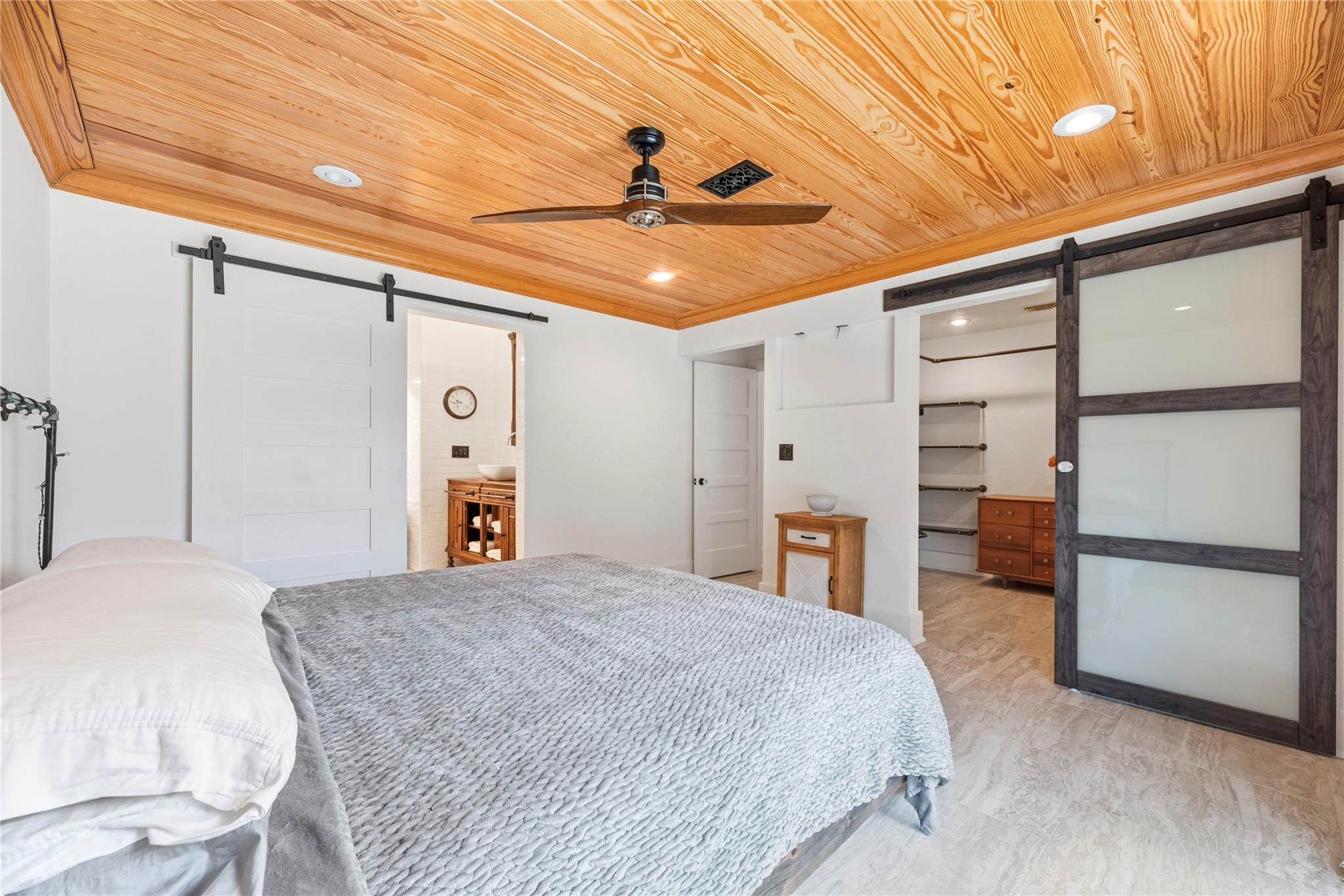 Bedroom with a wood-plank ceiling, sliding barn doors, and adjoining bathroom and closet.